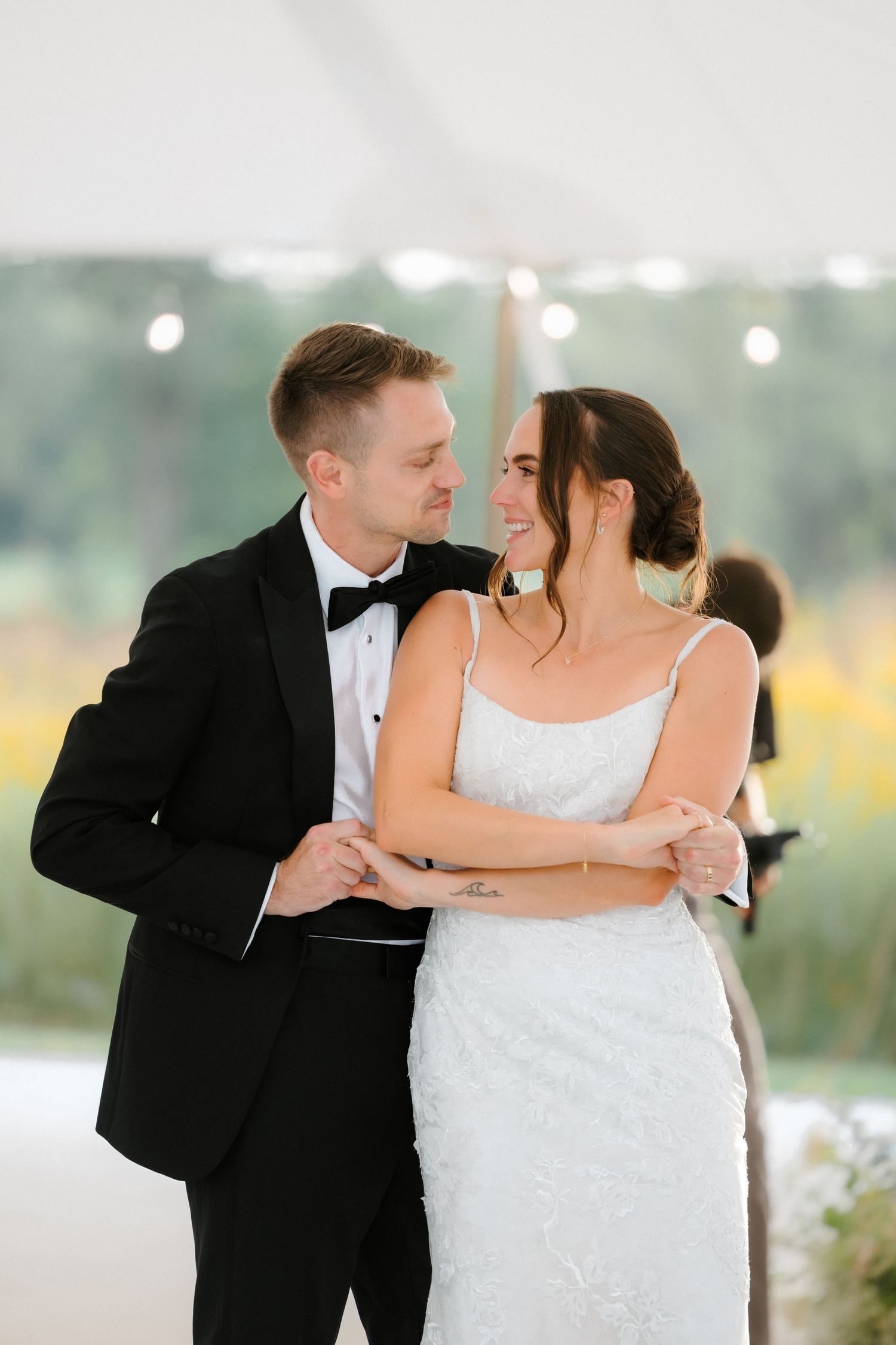 Smiling bride and groom share a tender moment during their first dance under a white wedding reception tent.