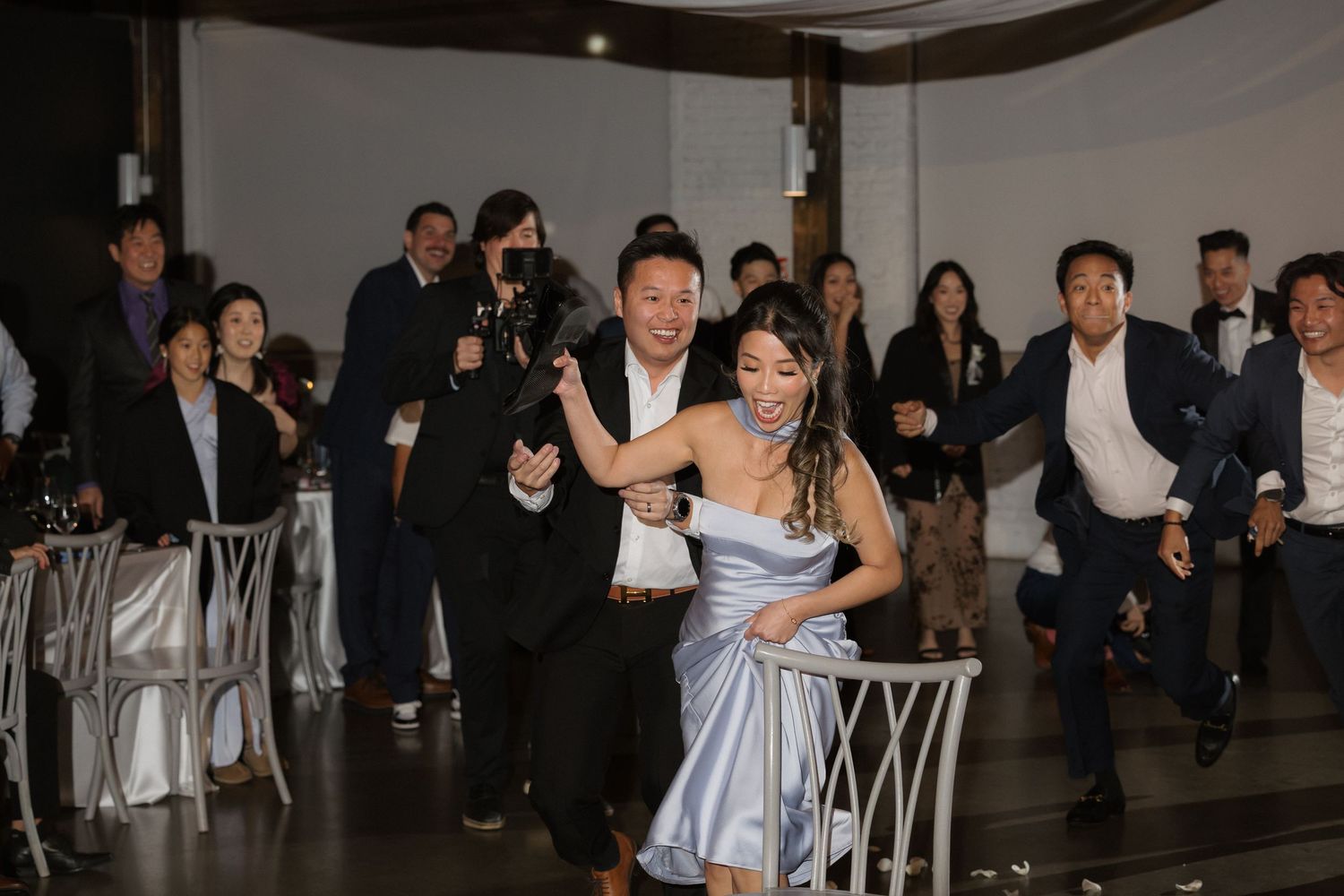 Wedding guests cheering and dancing energetically at a lively indoor wedding reception celebration.
