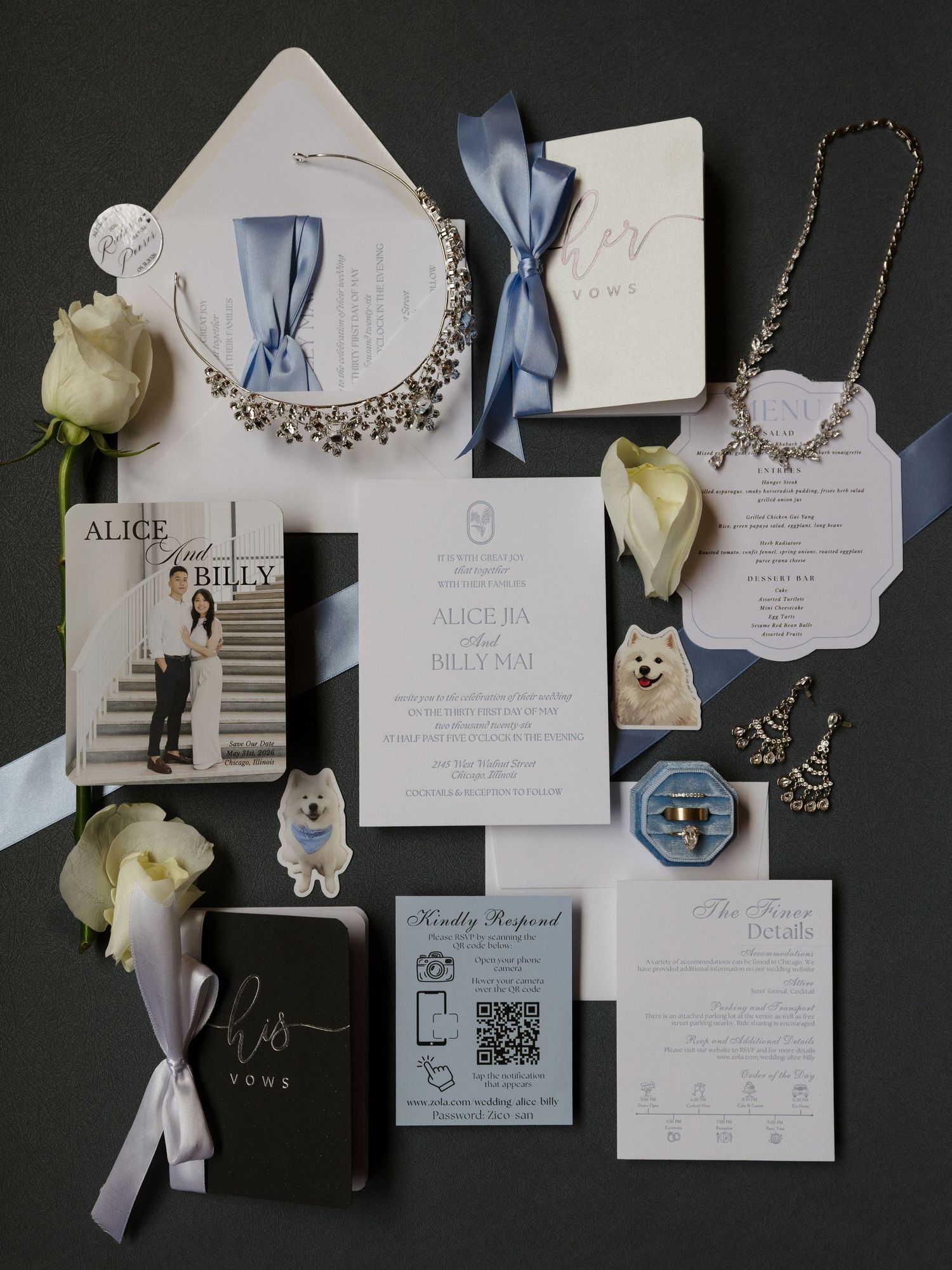 Elegant wedding invitation suite with dusty blue ribbons, floral accents, vow books, and jewelry on dark background.