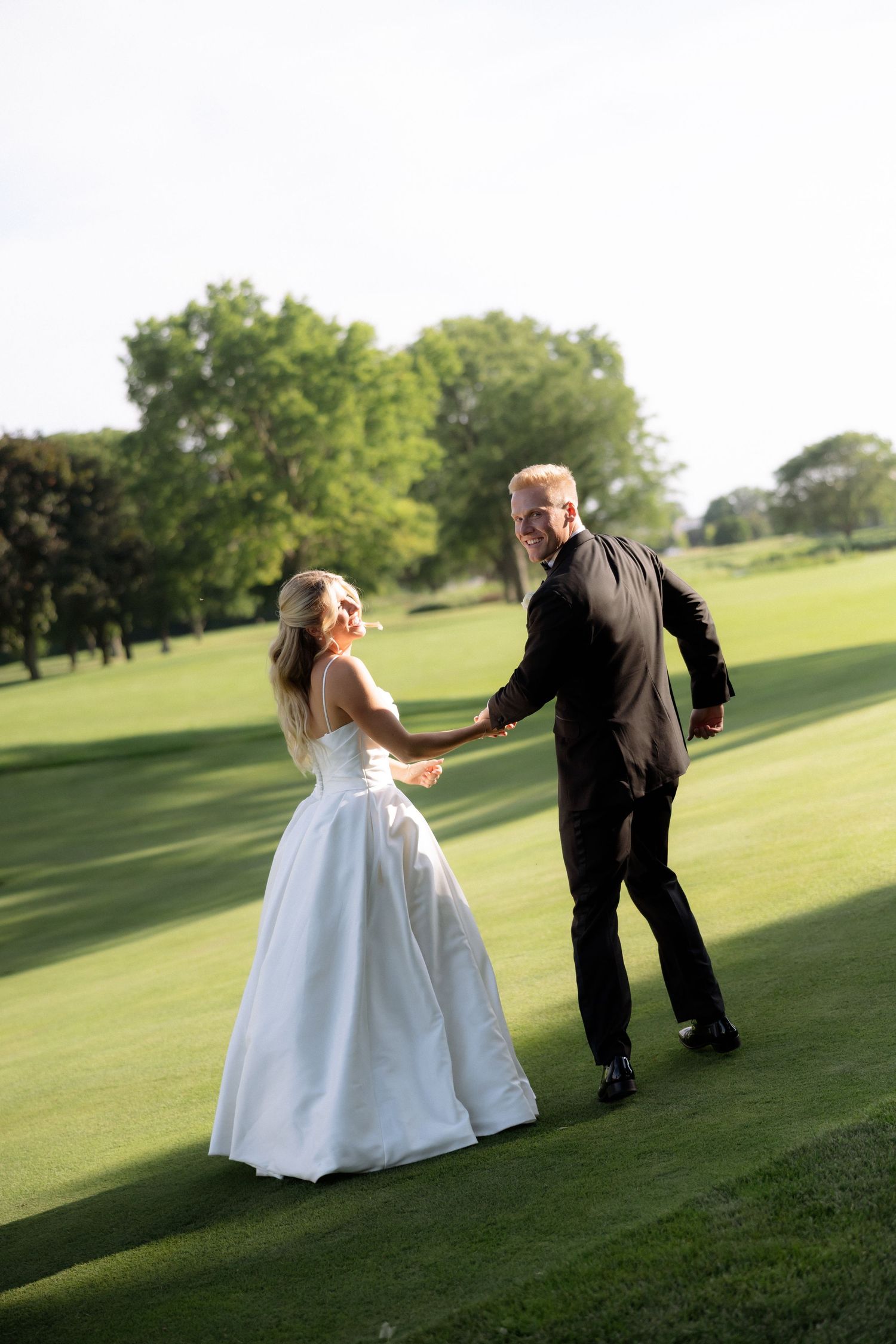 Smiling bride and groom dance together on a sunlit green golf course on their wedding day.