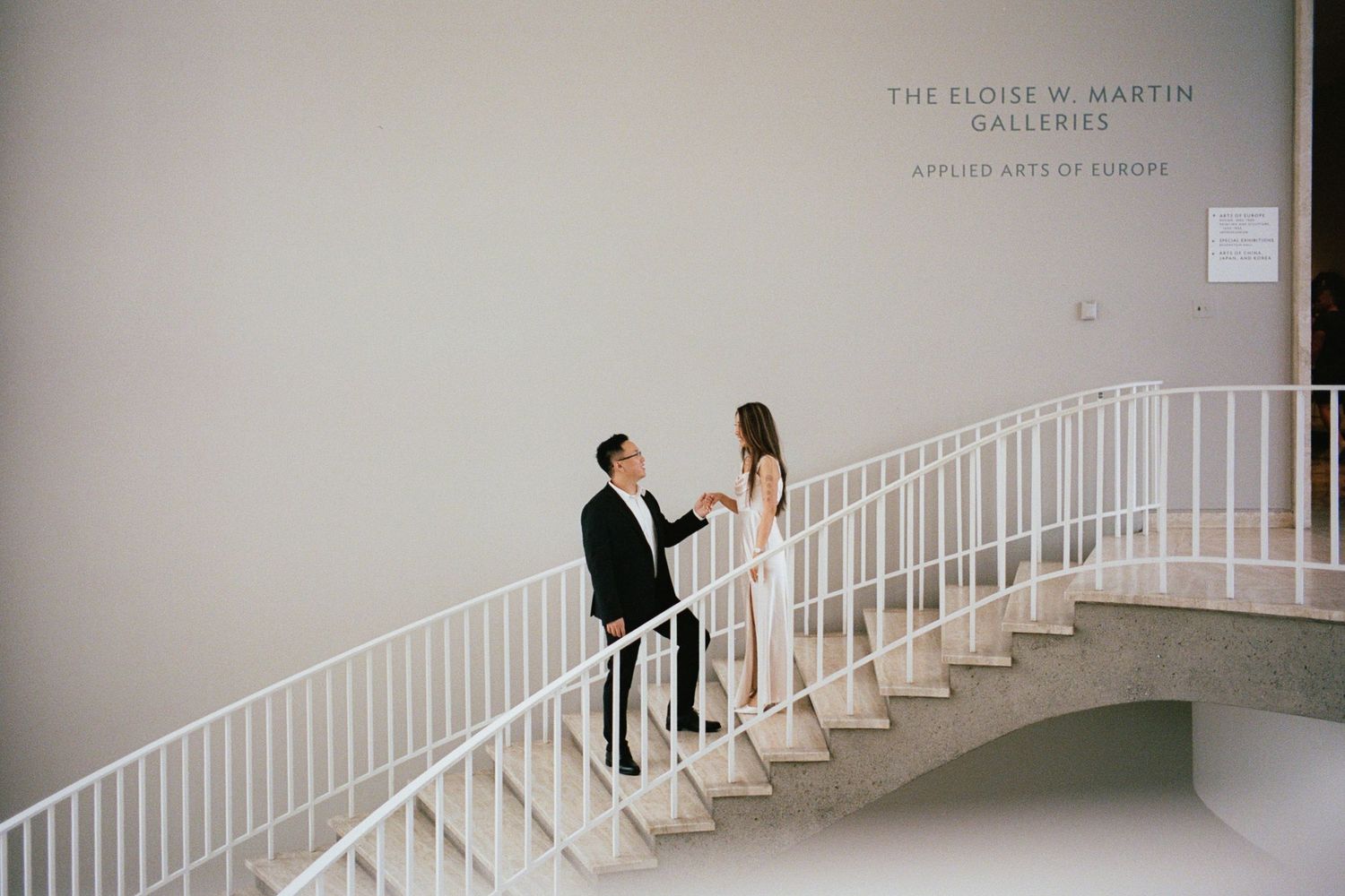 Couple in formal attire sharing a moment on white museum stairs at The Eloise W. Martyn Galleries.