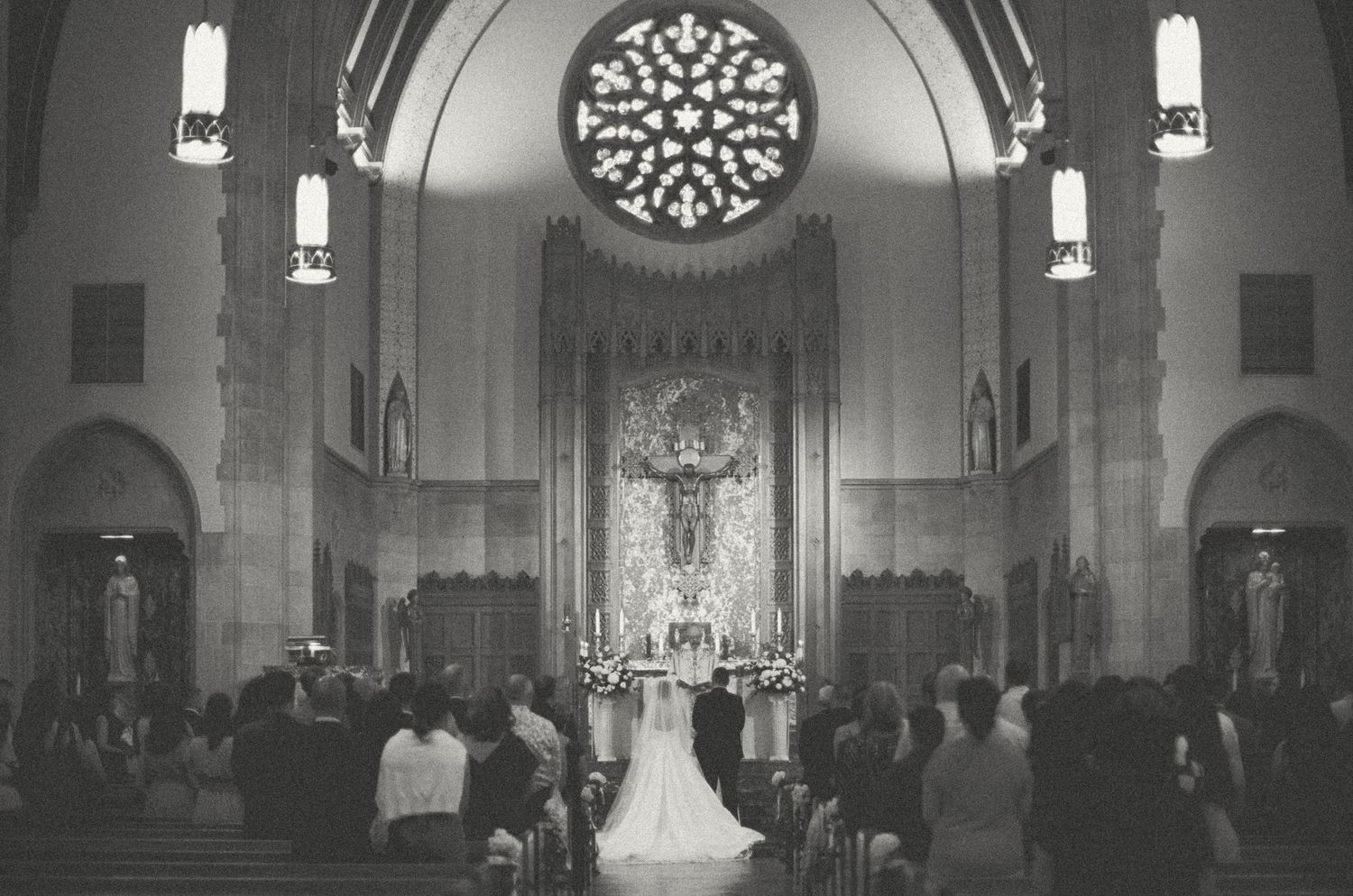 Black and white photo of a bride walking down the aisle in an ornate church with a rose window.