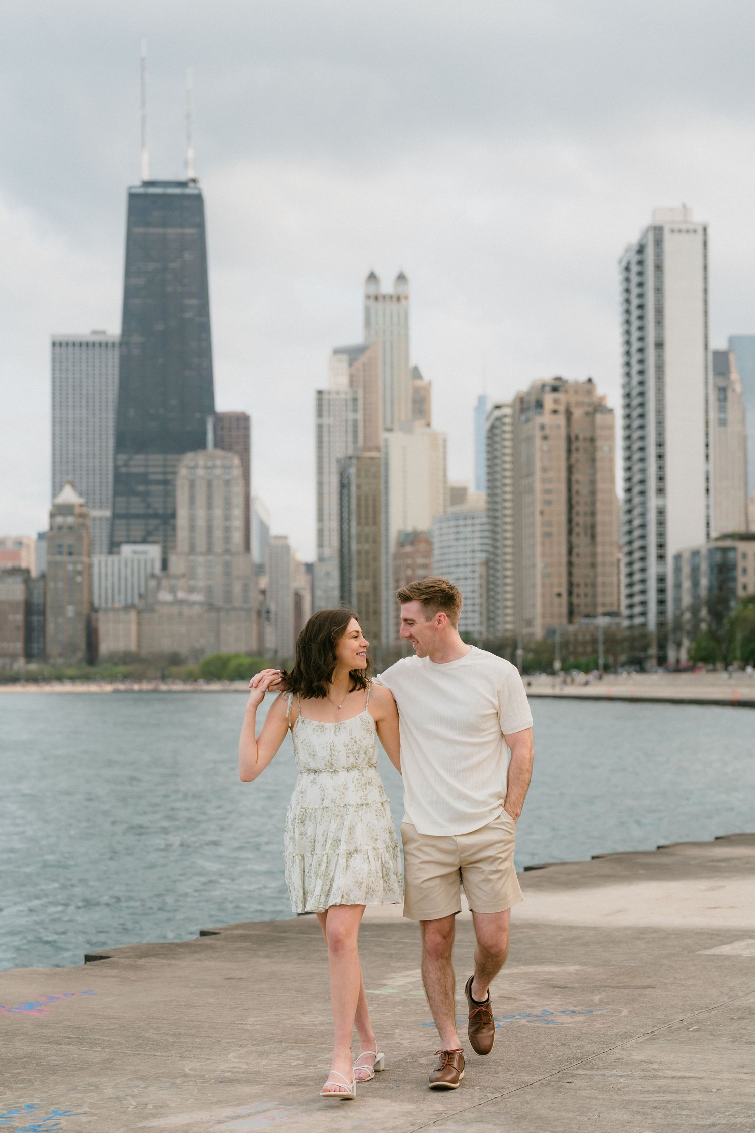 Couple walking and smiling together along Chicago lakefront pier with city skyline view.