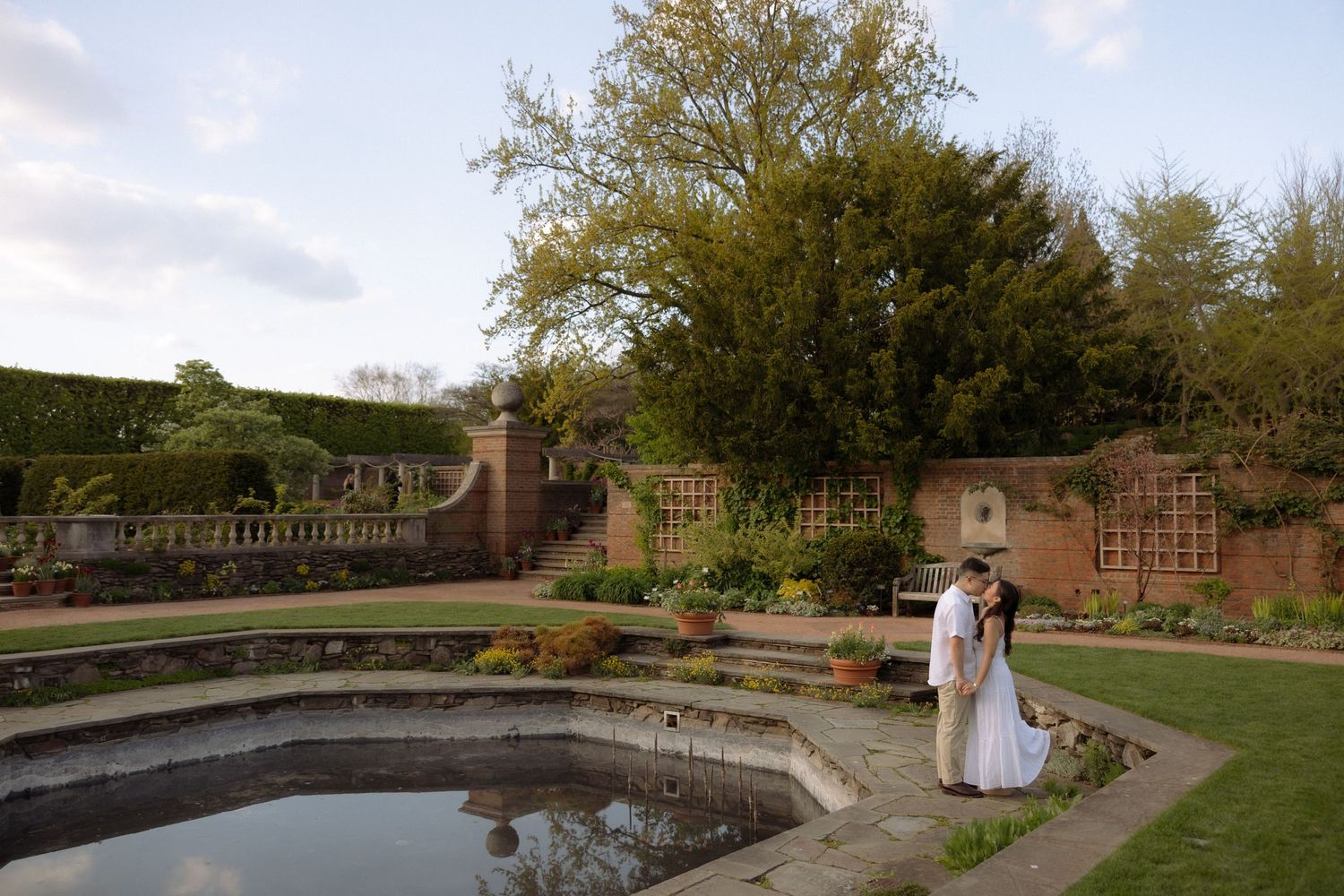 Bride and groom share a romantic moment by a garden pond at a historic walled estate wedding venue.
