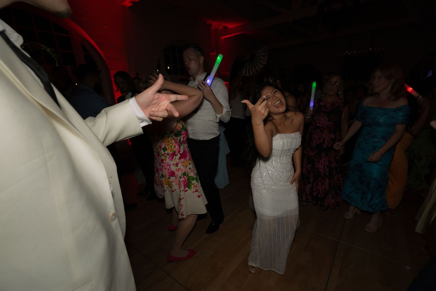 Guests dancing with glow sticks under red lighting at a lively late-night wedding reception dance floor.