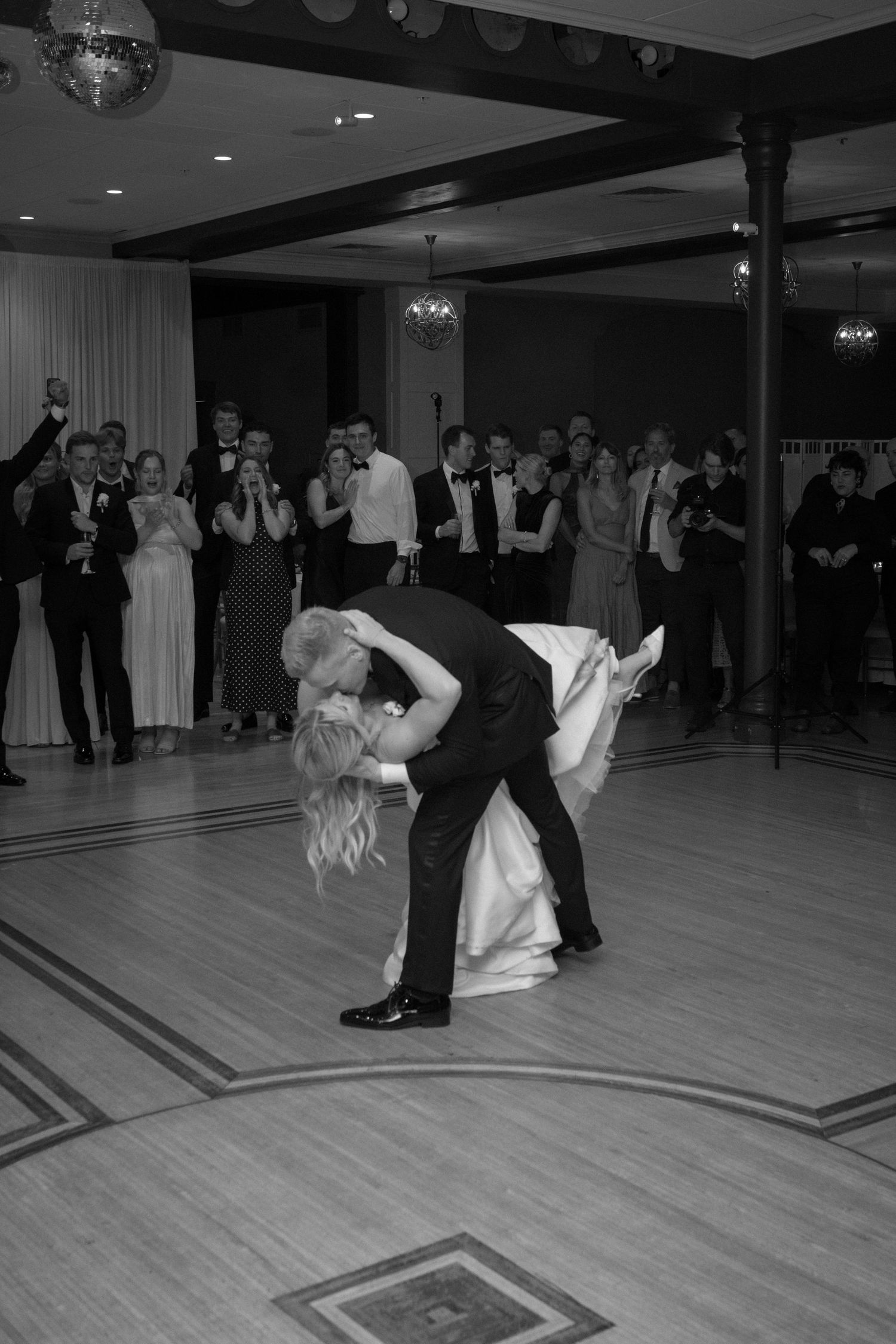 Groom dips bride for a kiss on dance floor during first dance at wedding reception in black and white.