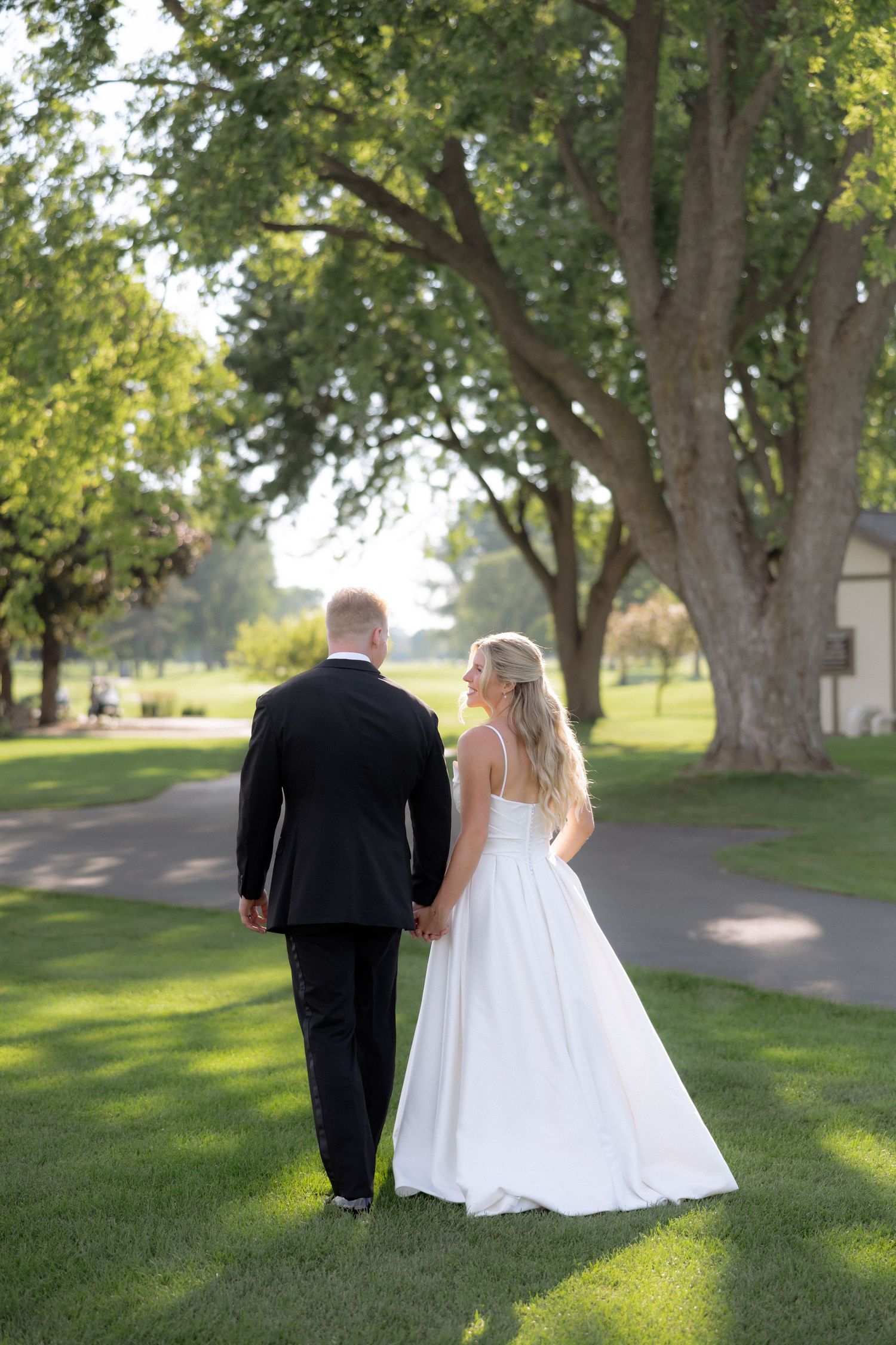 Bride and groom holding hands walking through lush green park on their wedding day.