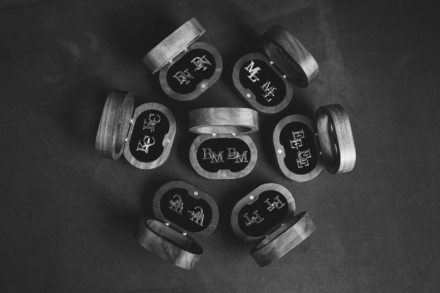 Black and white flat lay of seven small round cosmetic jars arranged in a circle on a dark background.