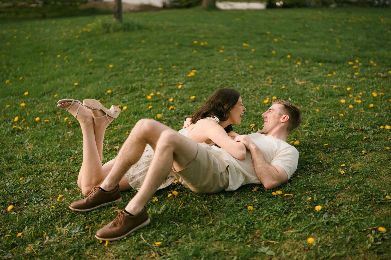 Couple laughing and cuddling together on green grass with yellow flowers.