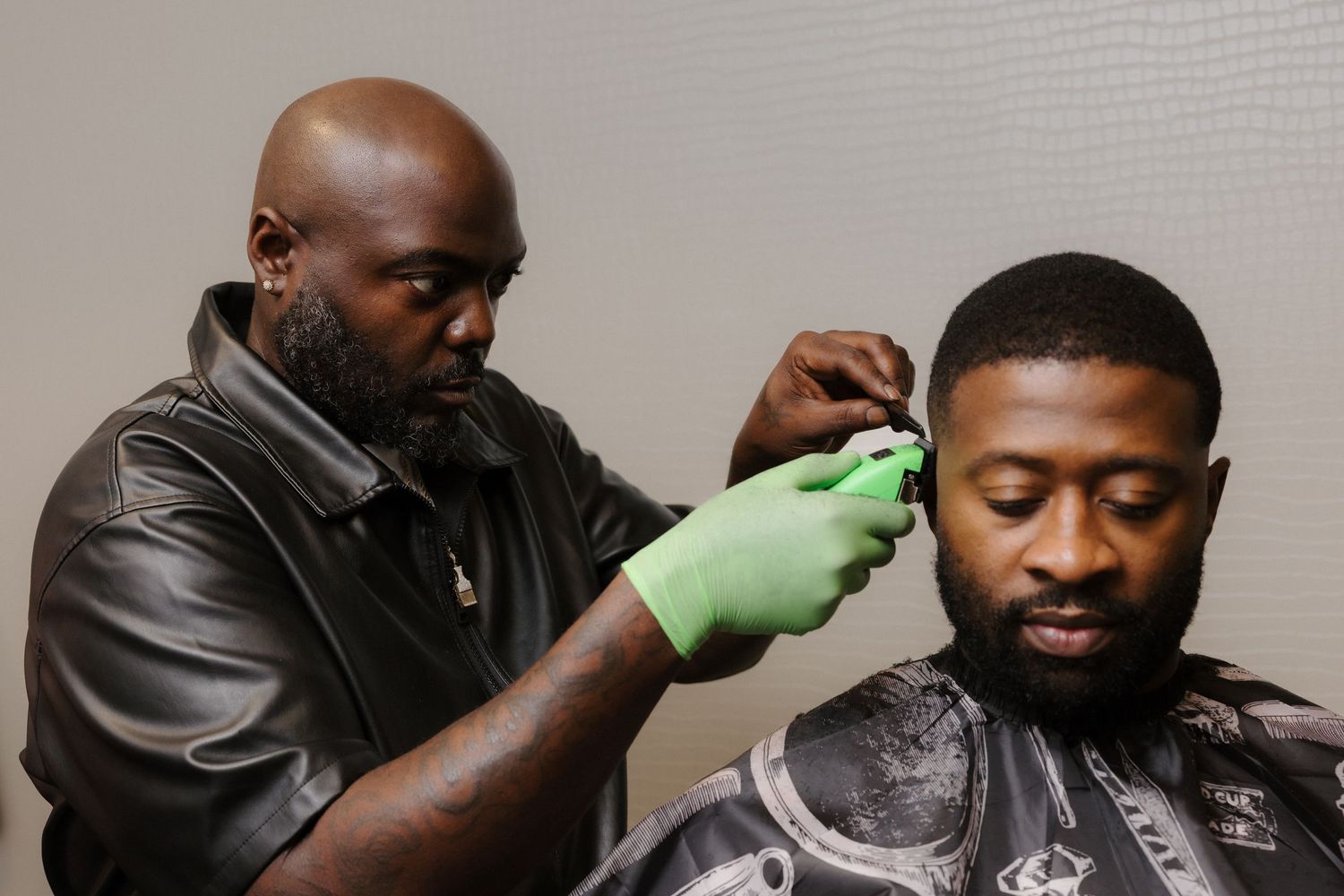 A barber wearing green gloves carefully cuts a client's hair in a professional barbershop setting.