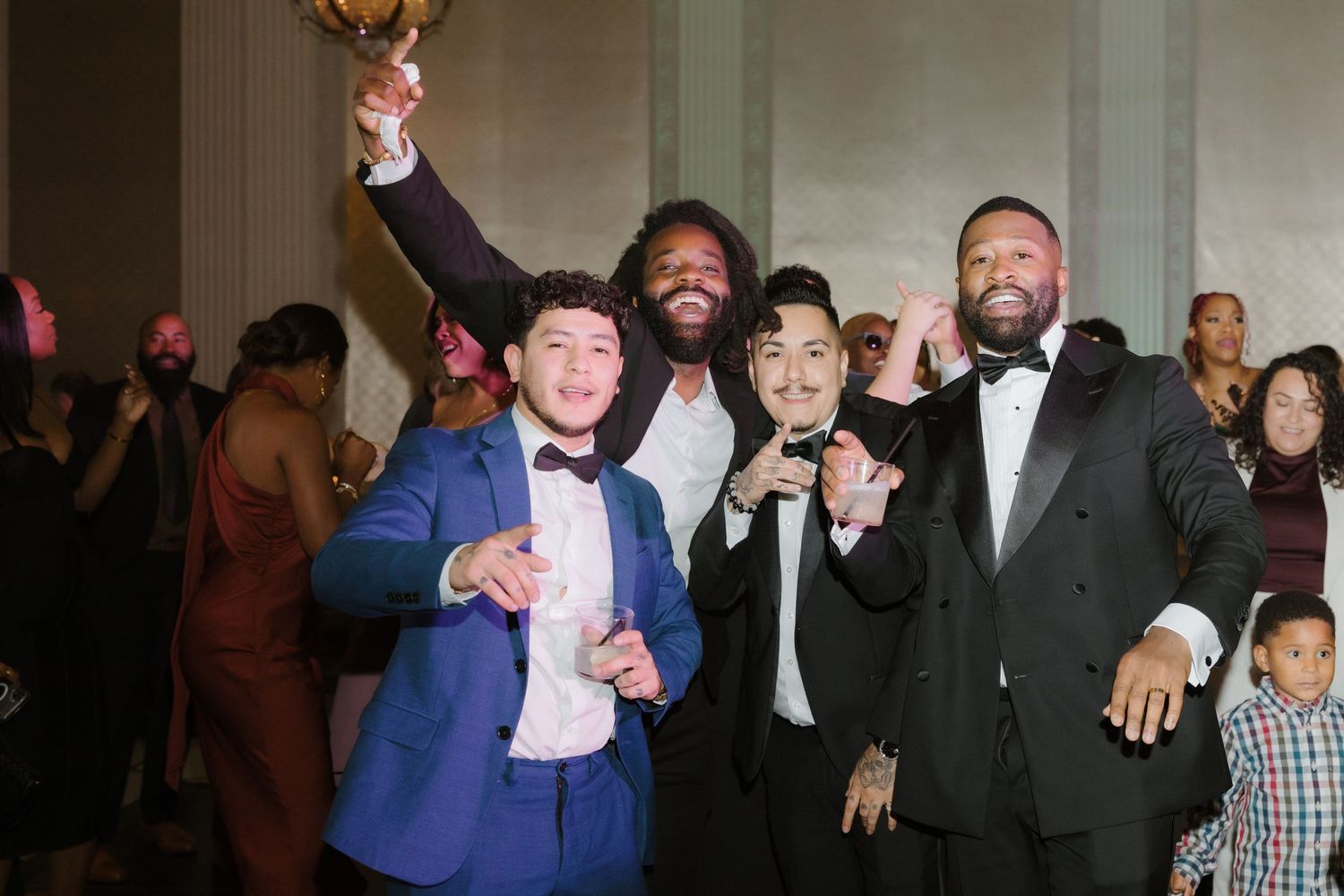 Group of men in formal attire smiling and posing together at an elegant evening celebration event.