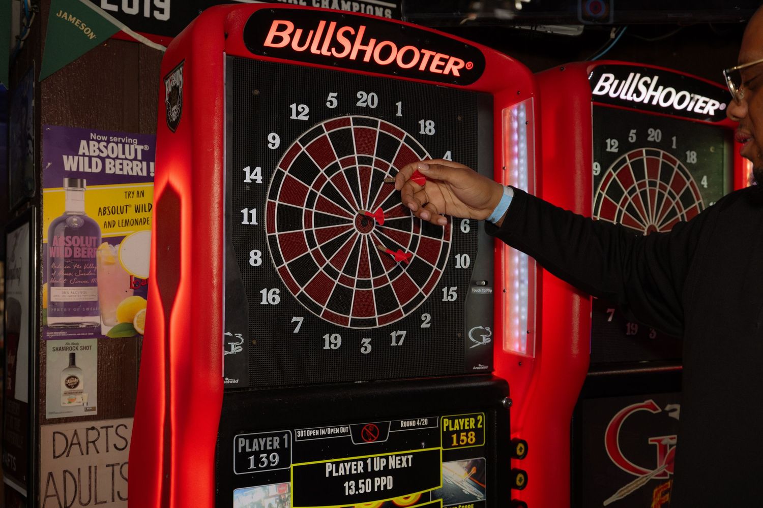 A person throwing a dart at a BullShooter electronic dartboard in a bar setting.