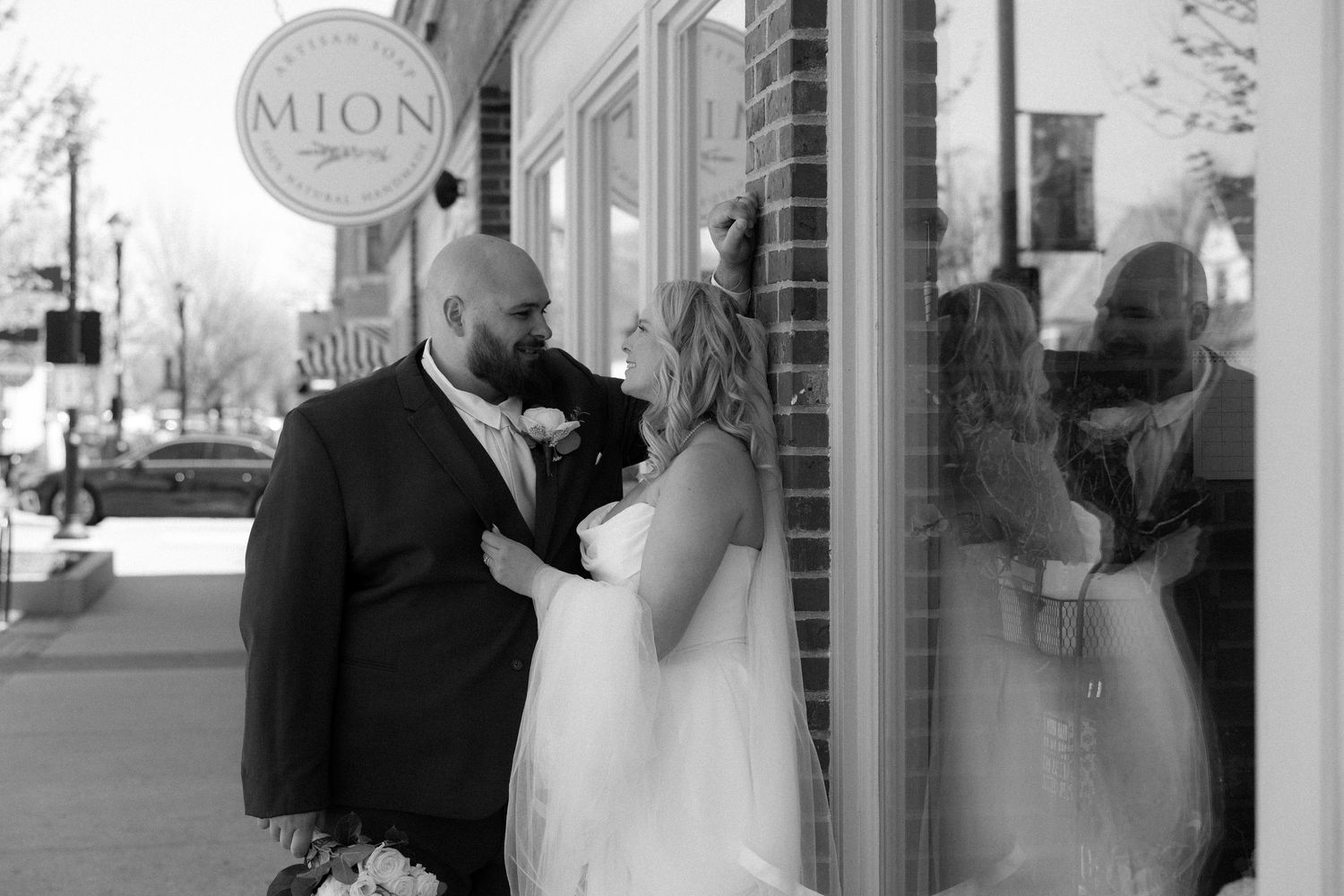 Black and white photo of a bride and groom sharing an intimate moment outside a MION storefront on their wedding day.