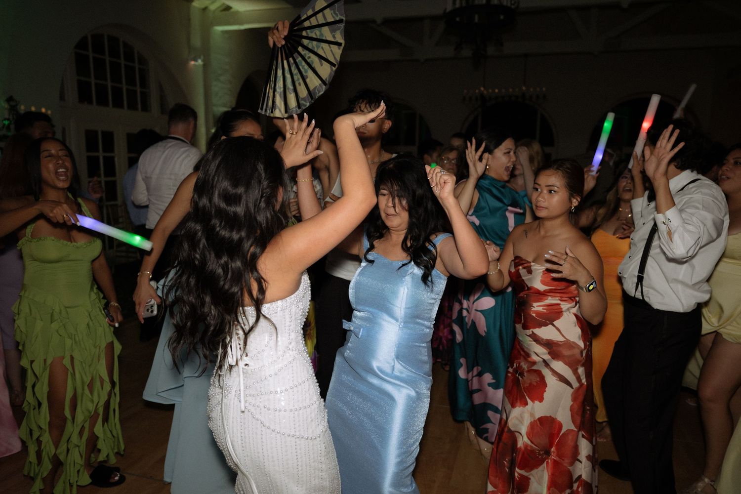 Wedding guests dancing energetically with glow sticks and fans at a vibrant reception party.