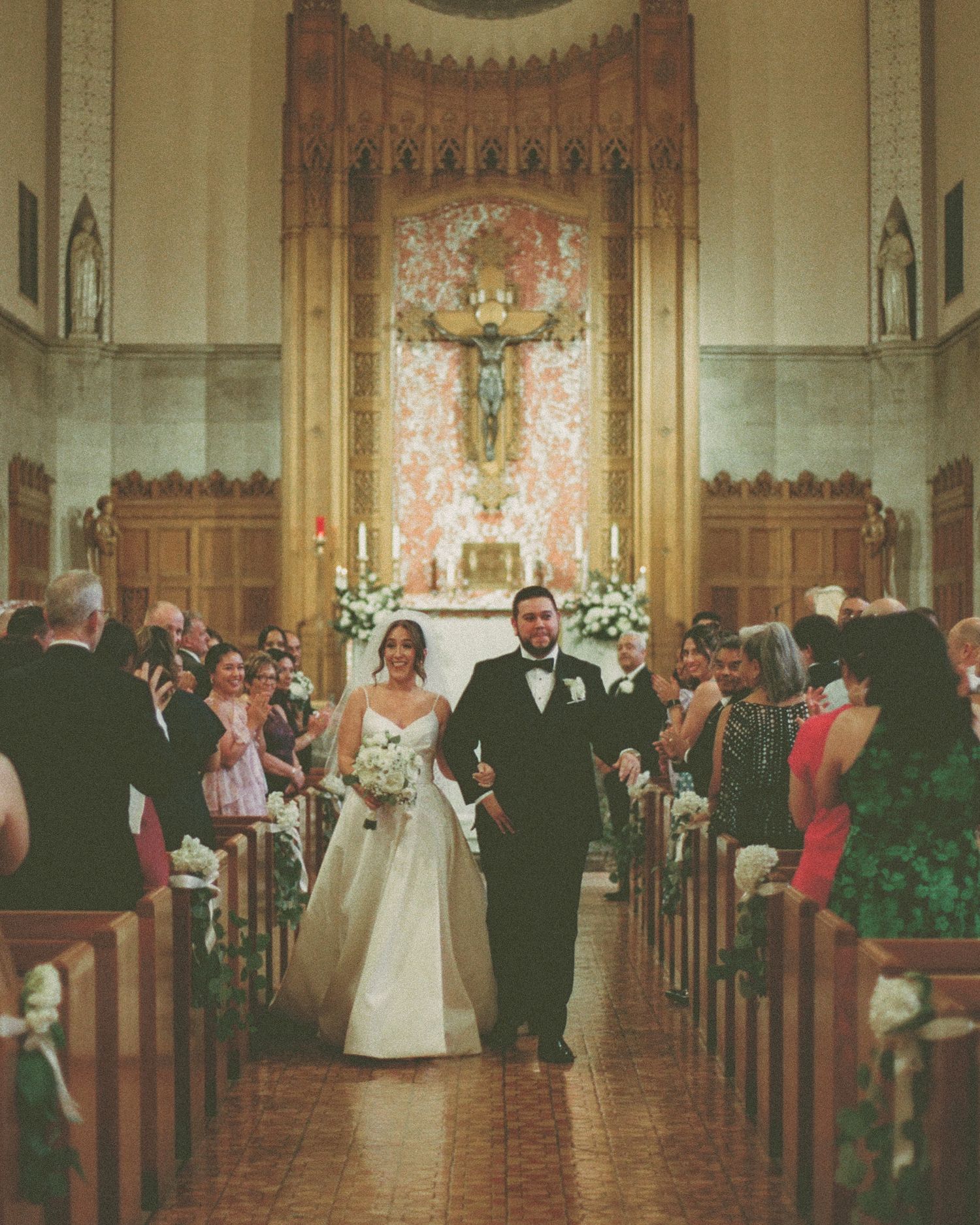 Bride and groom walk down the aisle of an ornate Catholic church after their wedding ceremony.