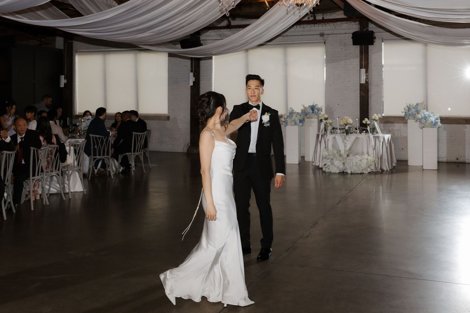 Bride and groom share their first dance in an elegant wedding reception venue with draped ceilings and soft blue decor.
