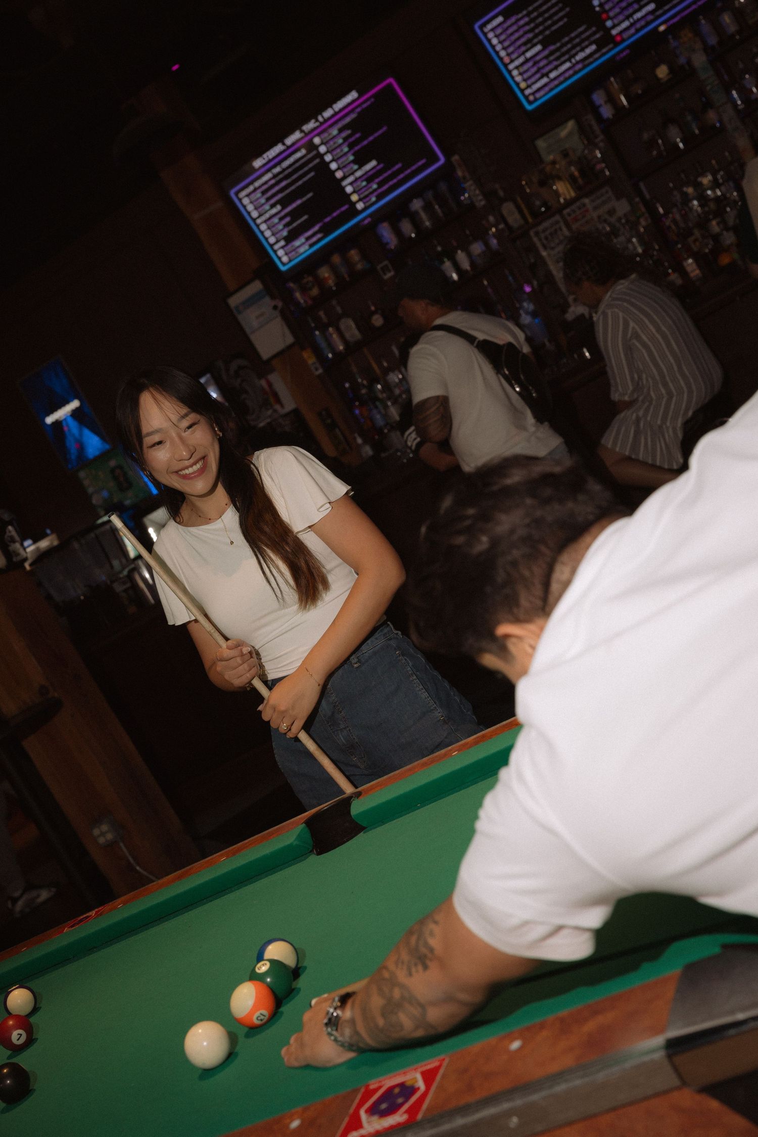 Young woman smiling while holding a pool cue at a bar billiards table.