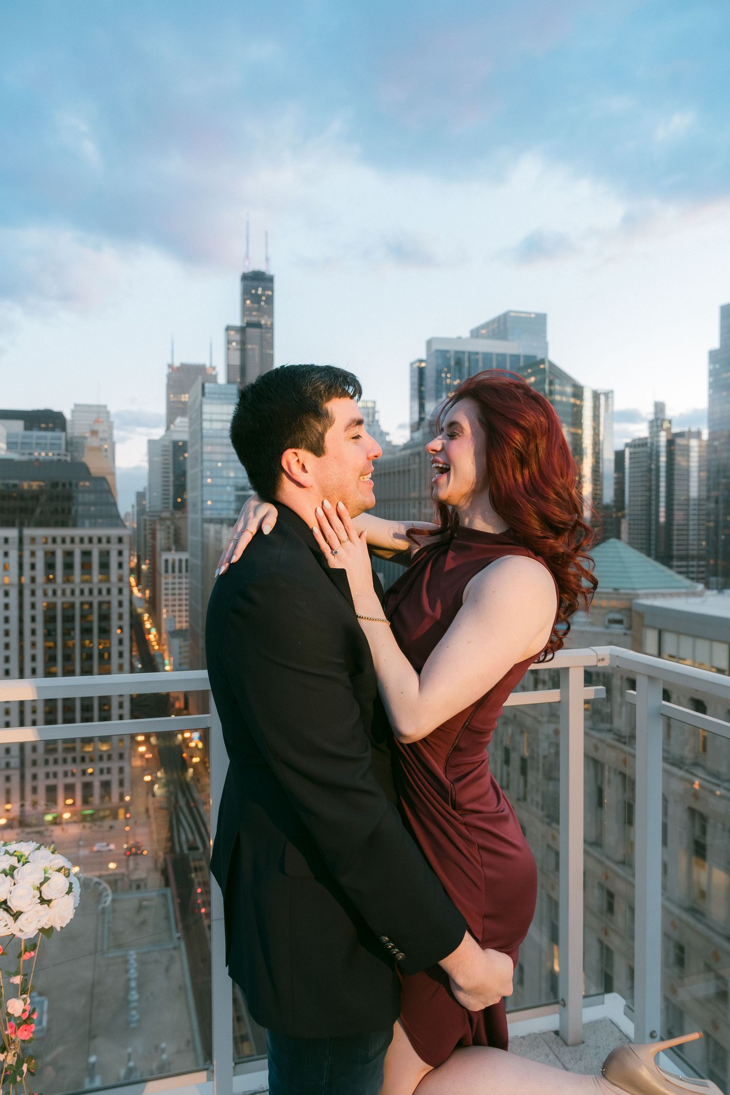 Joyful couple laughing together on Chicago rooftop with Willis Tower visible at dusk.