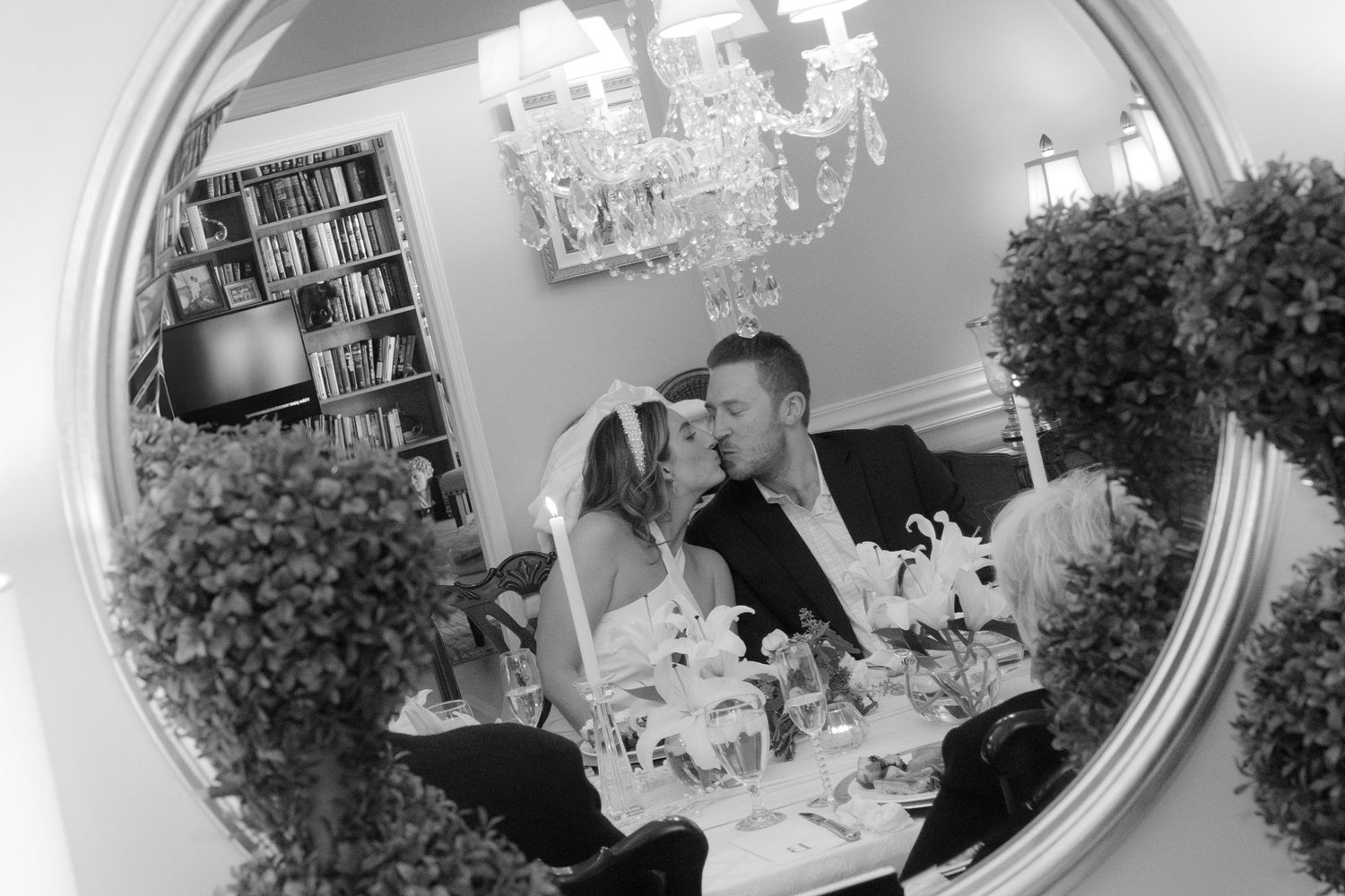 Black and white mirror reflection of newlywed couple sharing a kiss at their intimate wedding reception.