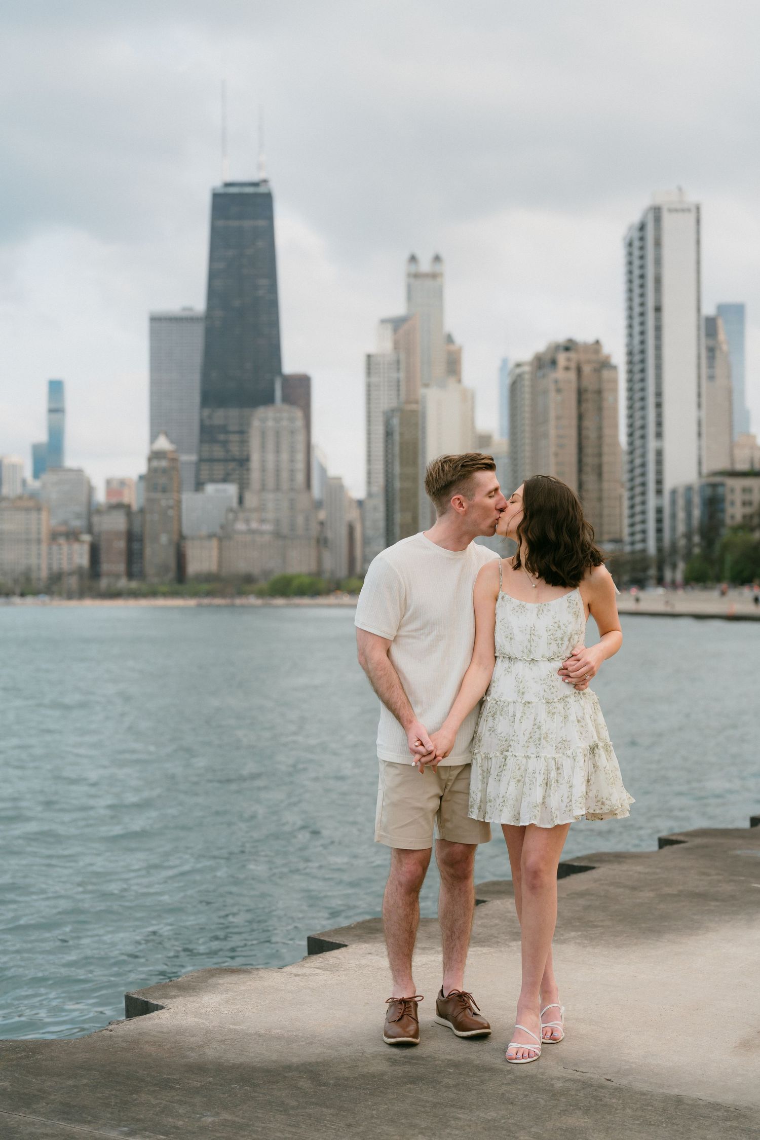 Couple sharing romantic kiss on waterfront pier with Chicago city skyline behind them.