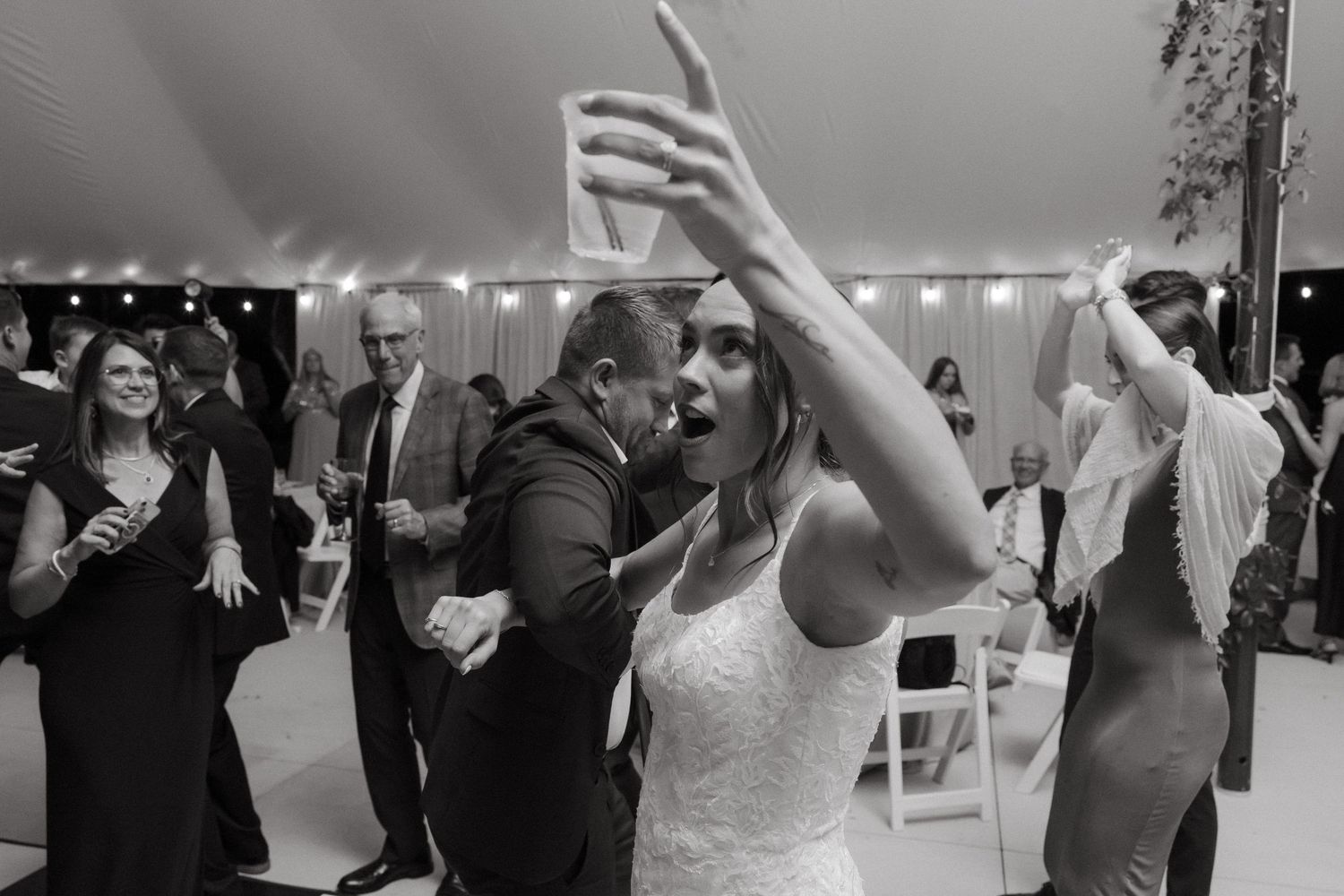 Bride dances energetically with guests on the dance floor at a lively wedding reception in black and white.