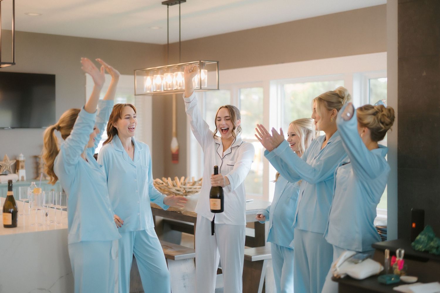 Bride and bridesmaids in matching light blue pajamas celebrating with champagne before the wedding.