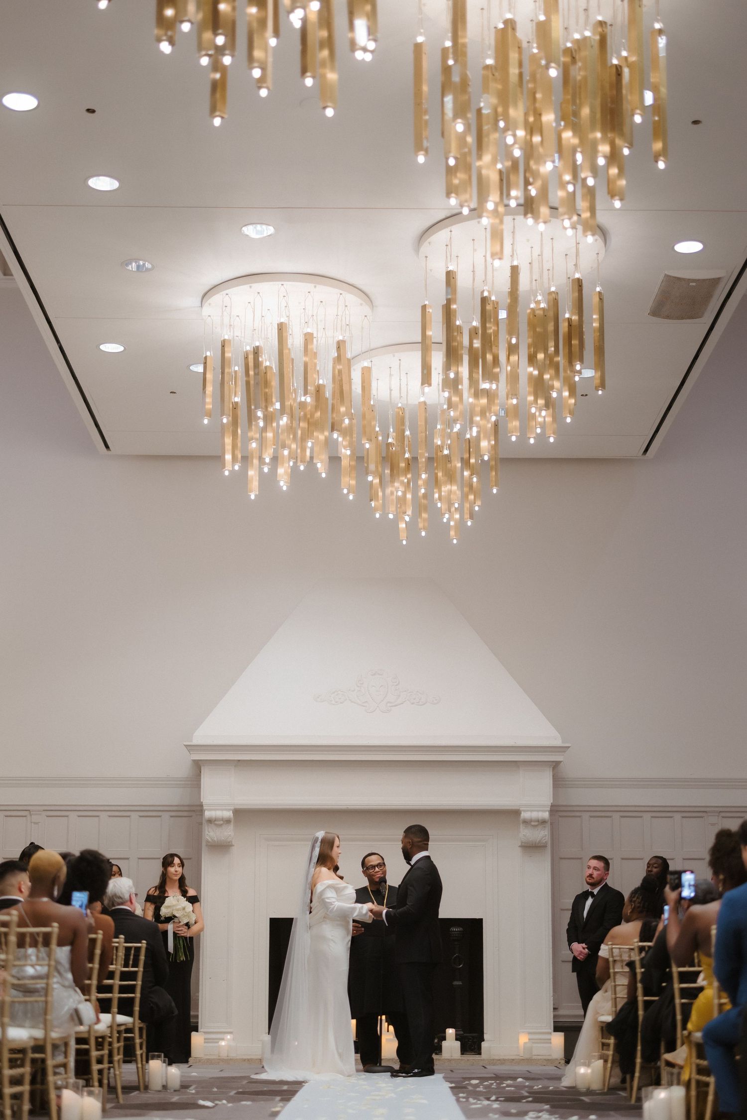 Couple exchanges vows under stunning gold chandelier at indoor wedding ceremony.