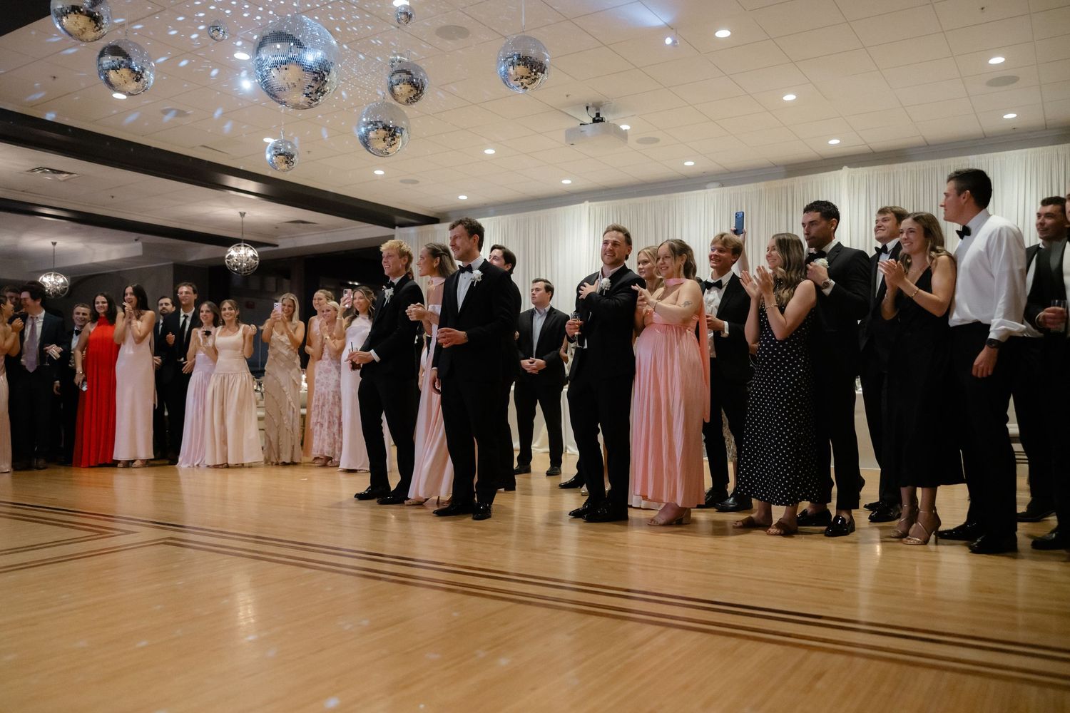Wedding guests line the dance floor during a lively celebration at an elegant reception venue.