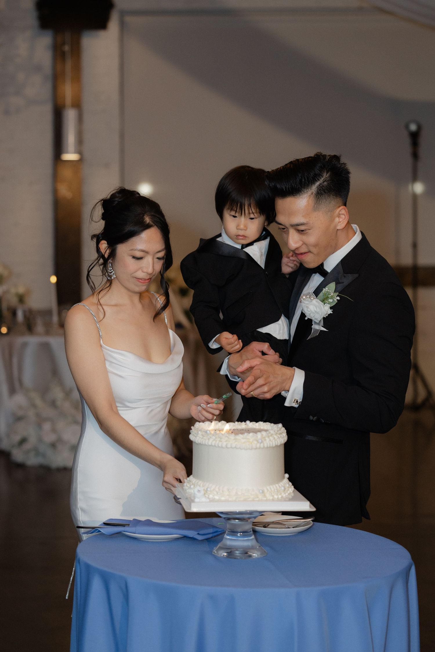 Bride and groom with toddler cut white wedding cake at reception.