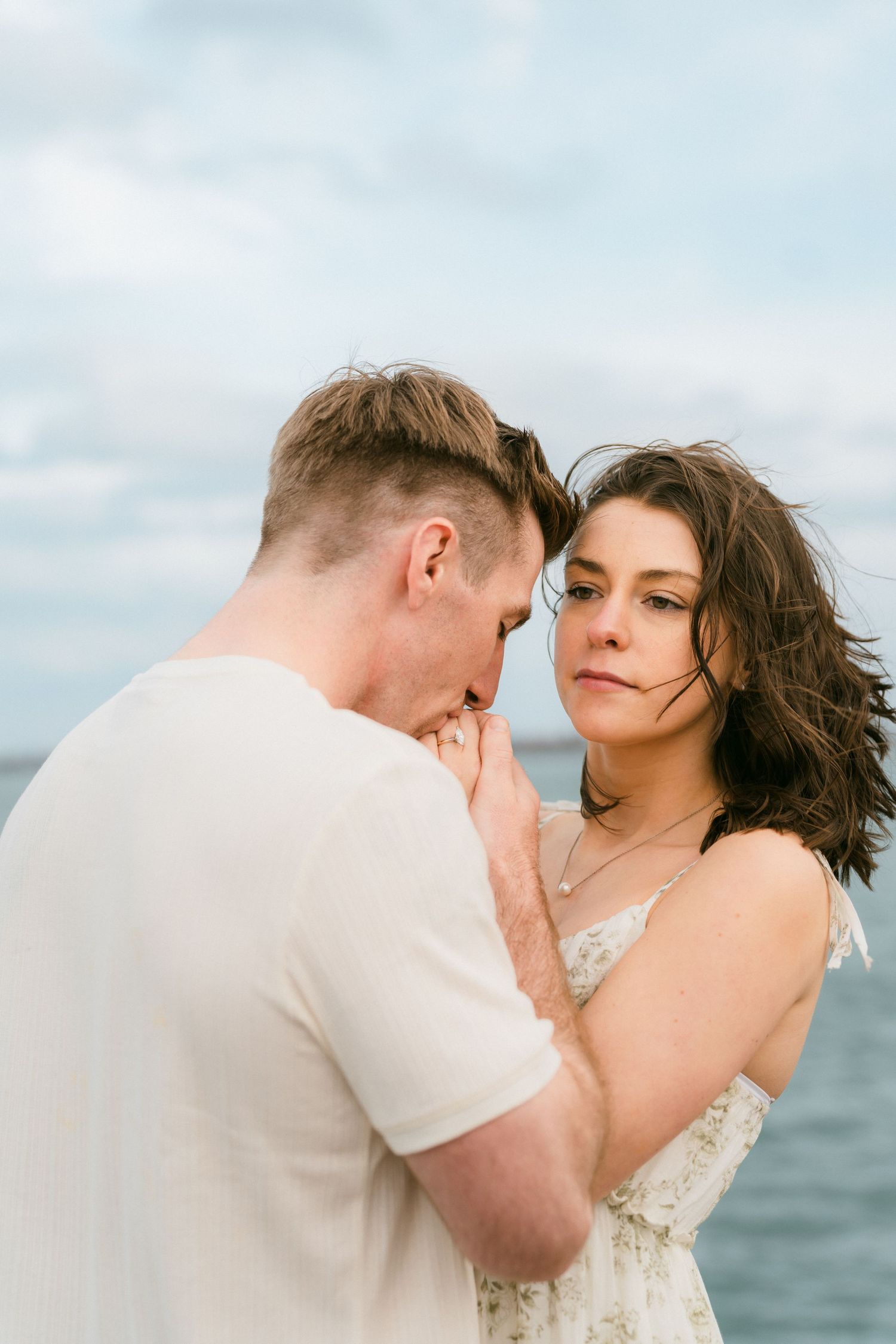 Tender couple moment as man kisses woman's hand by the seaside on a cloudy day.