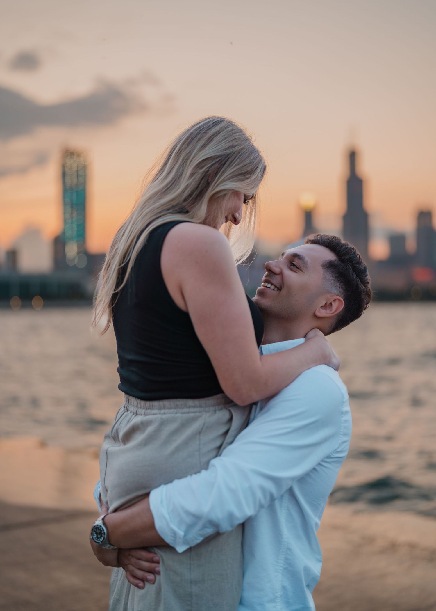 Couple embracing at sunset with Chicago skyline and lake in the background, romantic outdoor portrait.