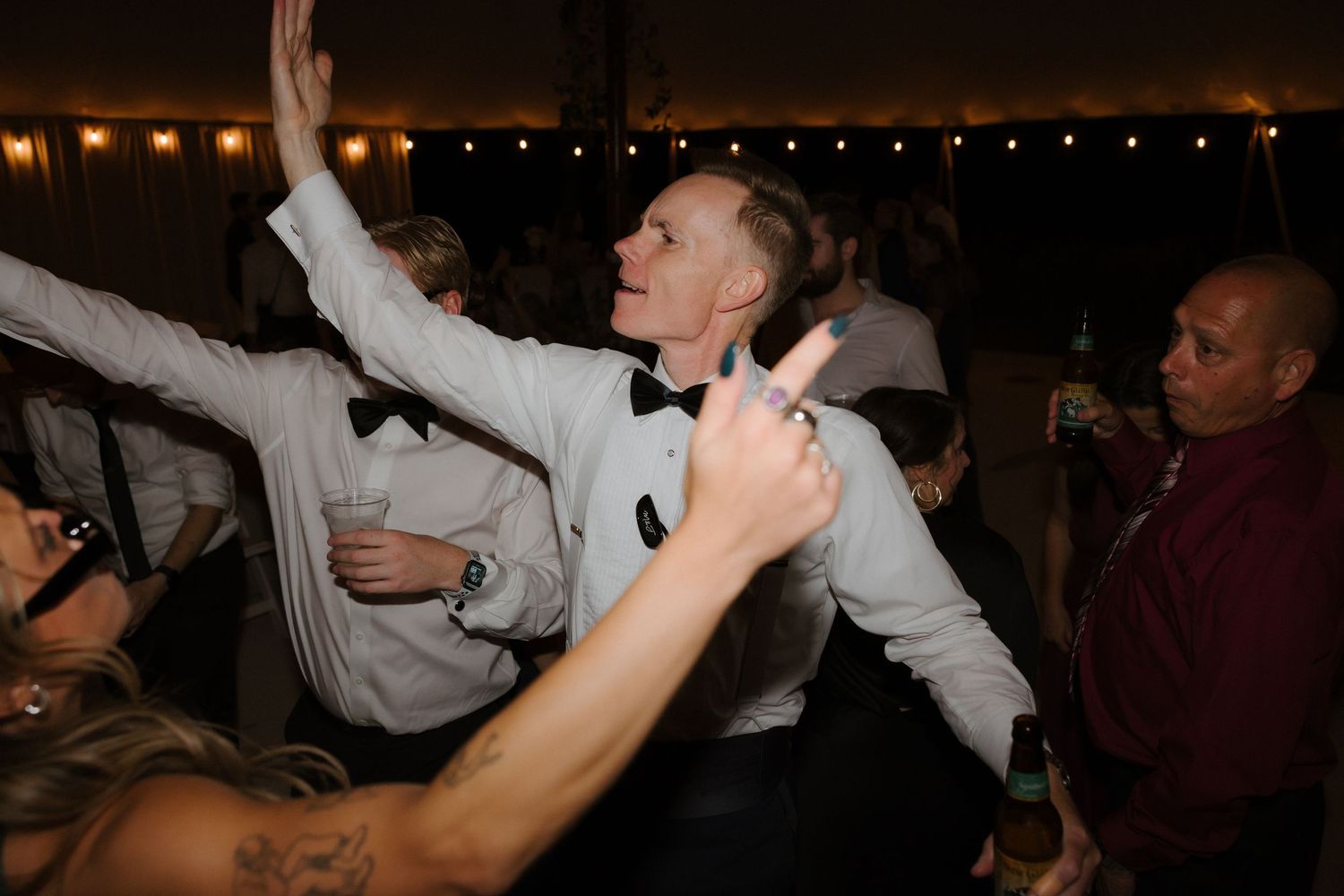 Energetic wedding guest in white tuxedo dancing with arms raised at a lively reception party.