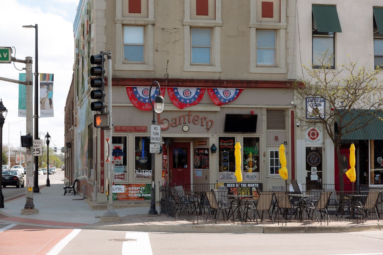 Corner bar restaurant with patriotic bunting decorations, outdoor seating, and traffic lights at a city intersection.