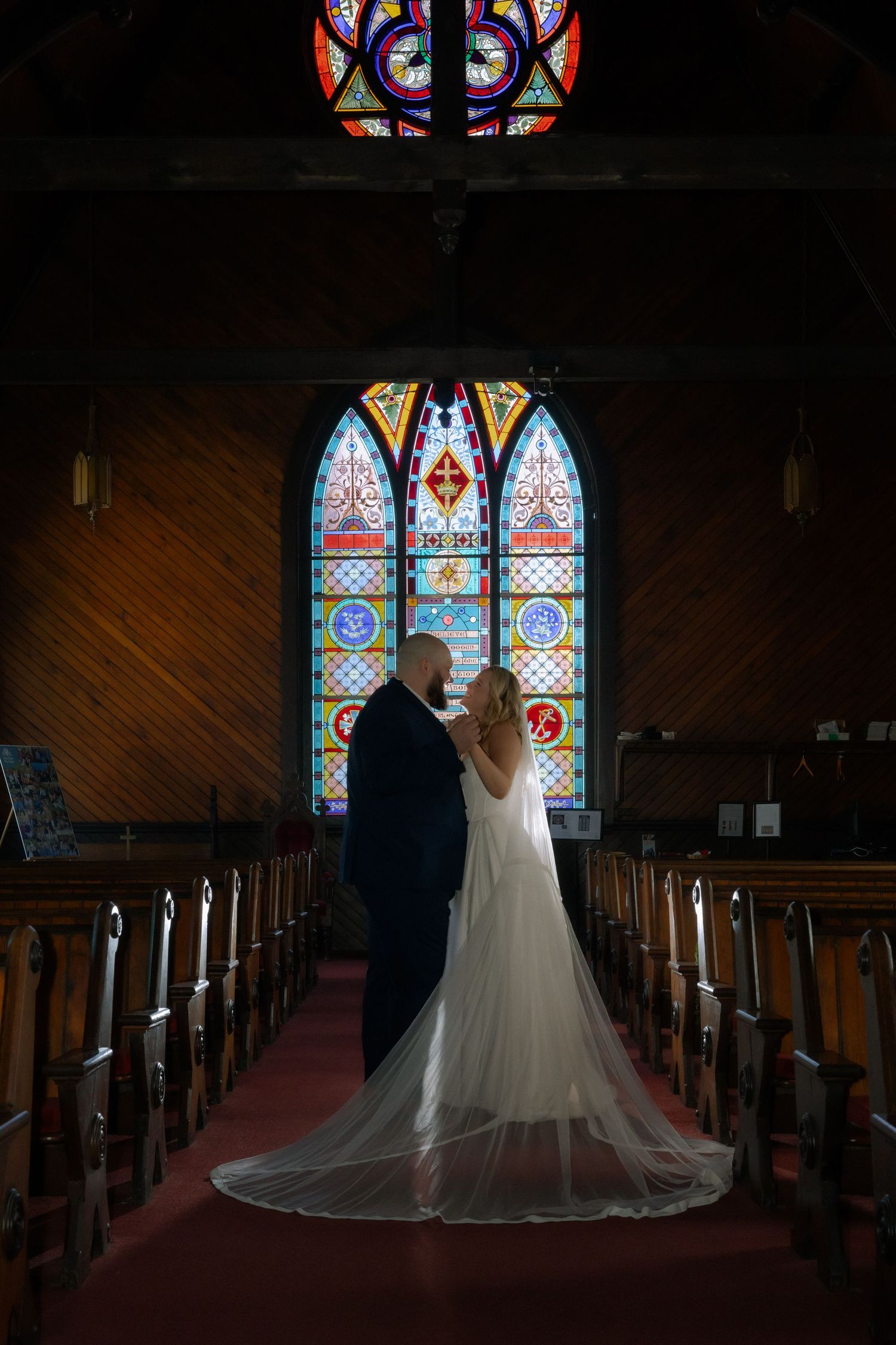 Bride and groom share a romantic moment at the altar of a church with stunning colorful stained glass windows.