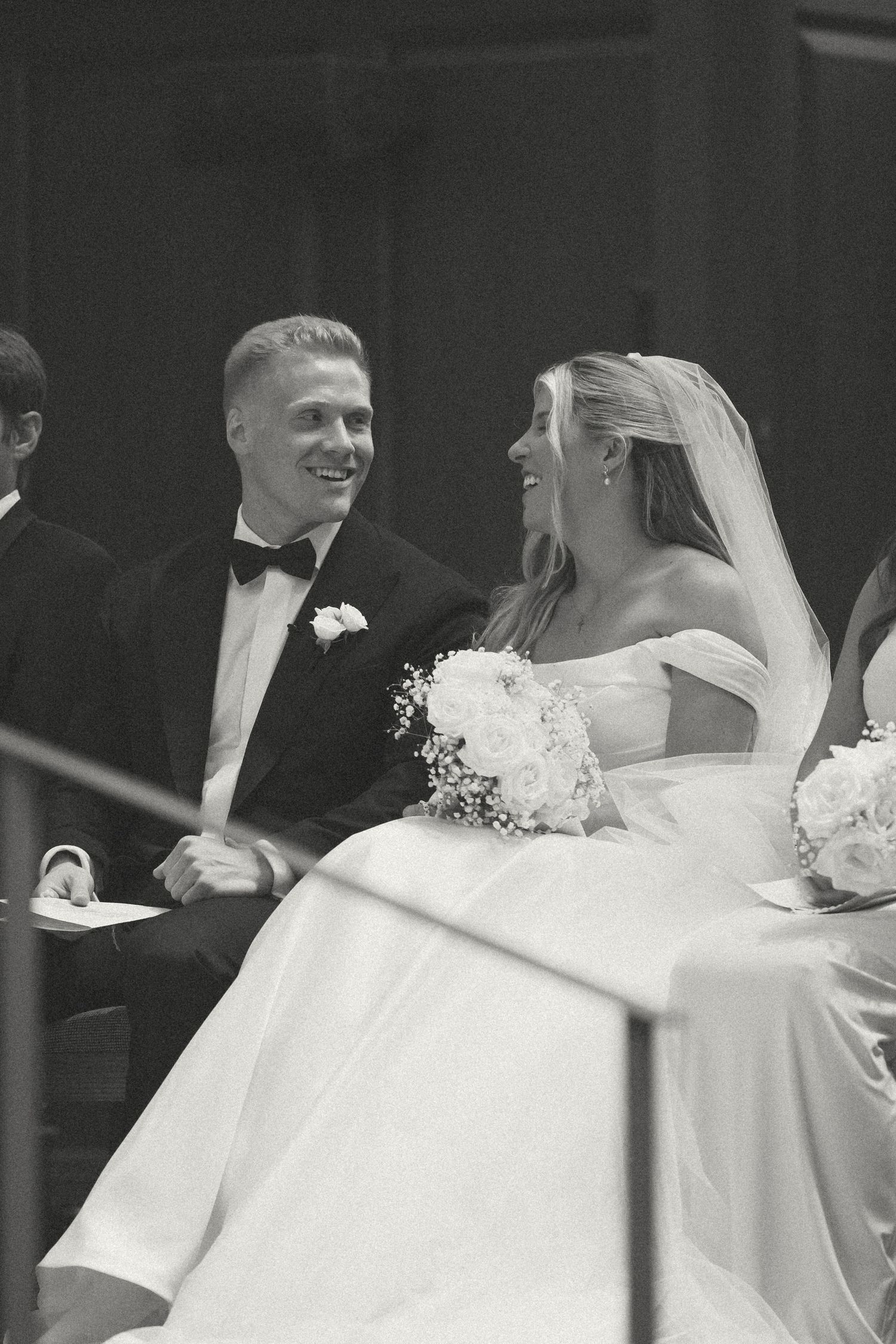 Black and white photo of a smiling bride and groom holding hands during their wedding ceremony.