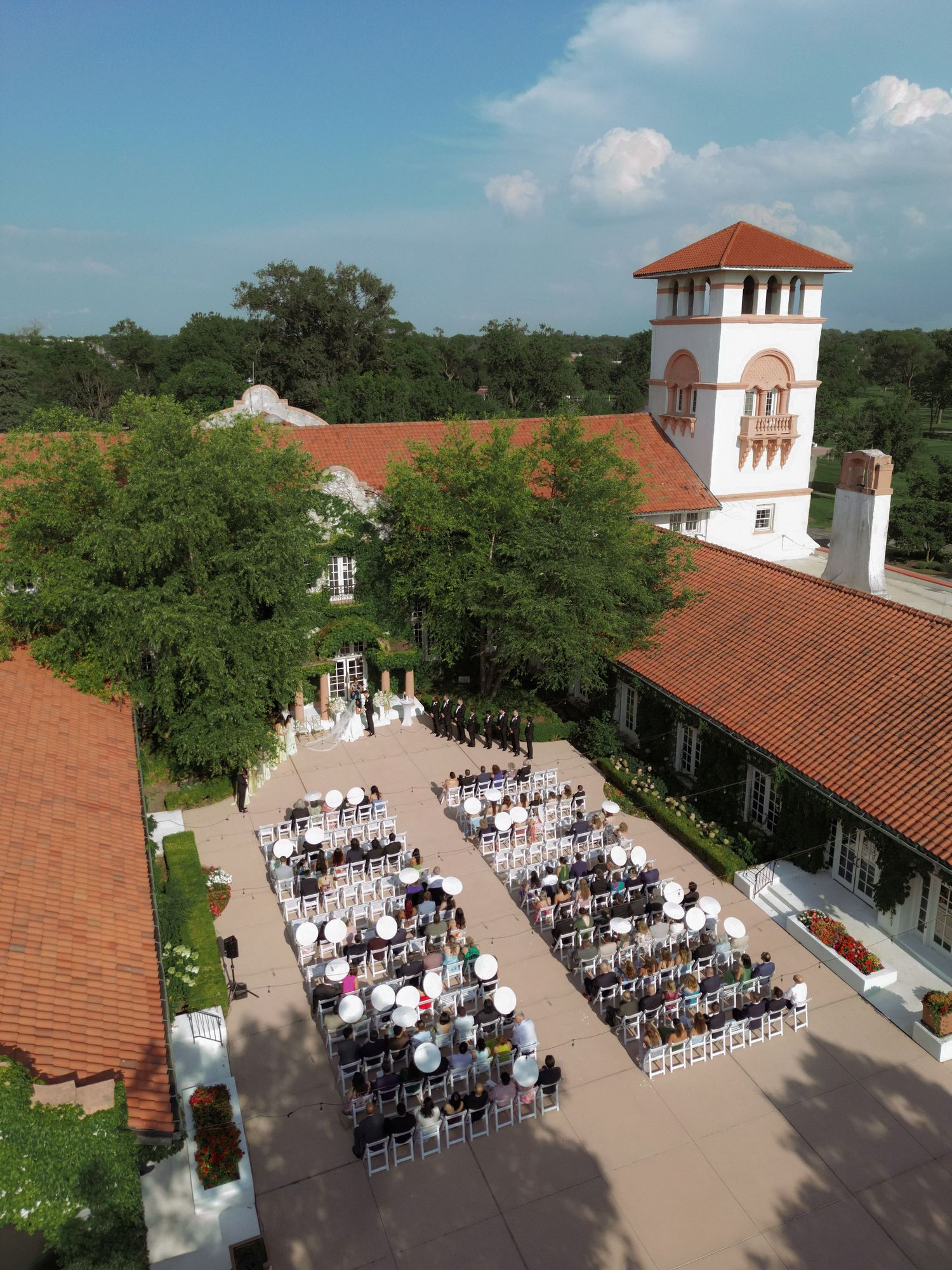 Aerial view of outdoor wedding ceremony with white chairs arranged in rows at a Spanish-style estate.