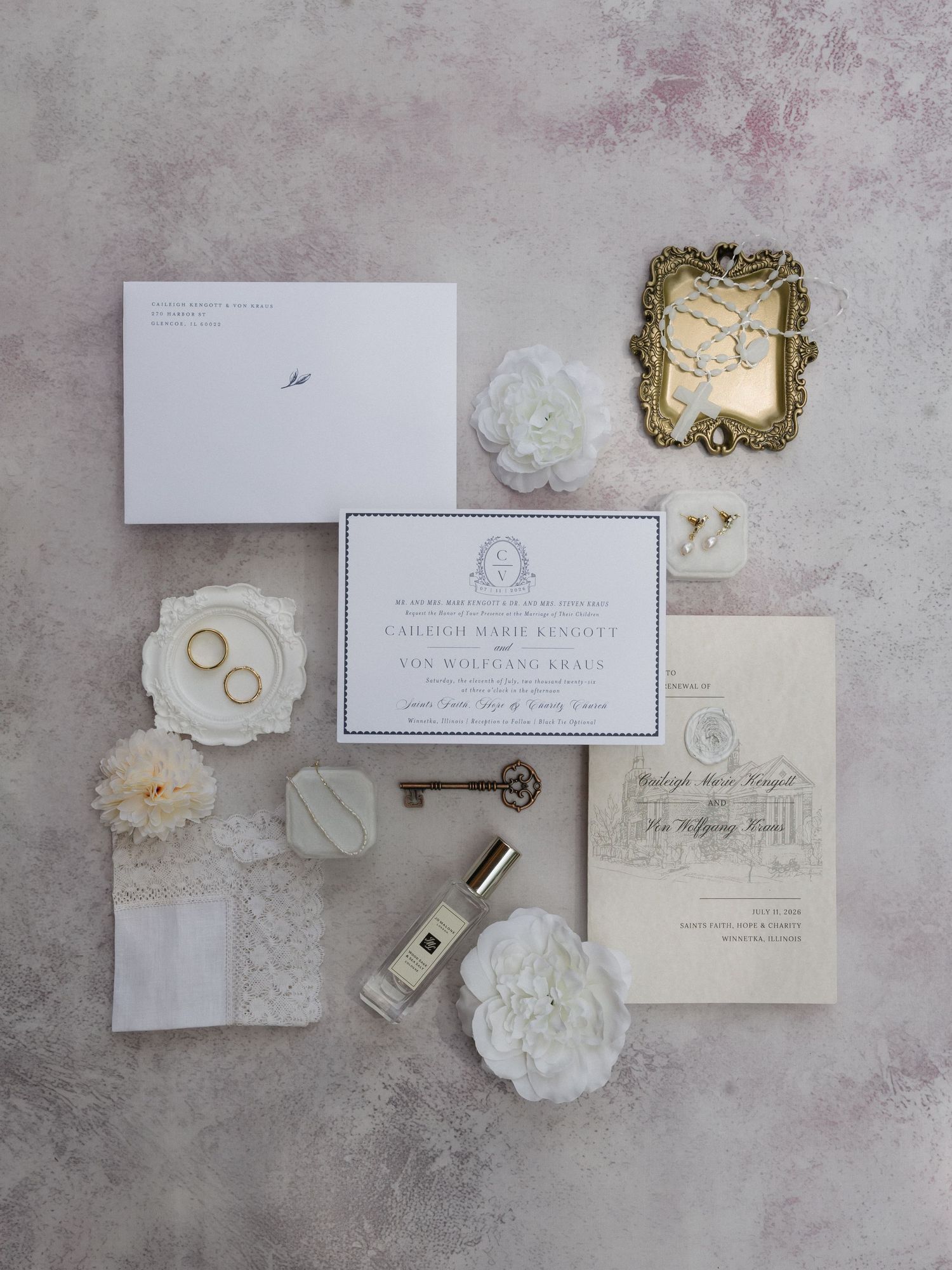 Elegant wedding invitation suite with white florals, gold mirror, vintage key, and Jo Malone perfume on marble surface.