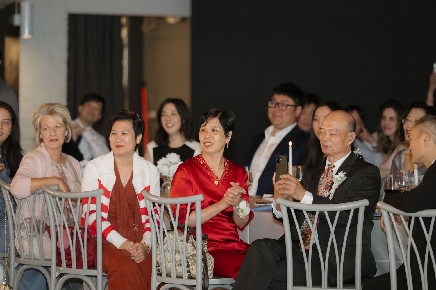 Wedding guests smiling and raising glasses during a celebratory toast at a formal reception dinner.