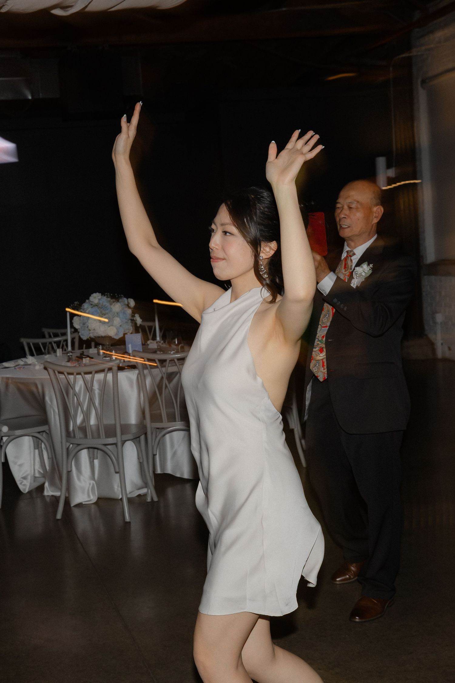 Woman in white dress dancing with arms raised at an elegant wedding reception.