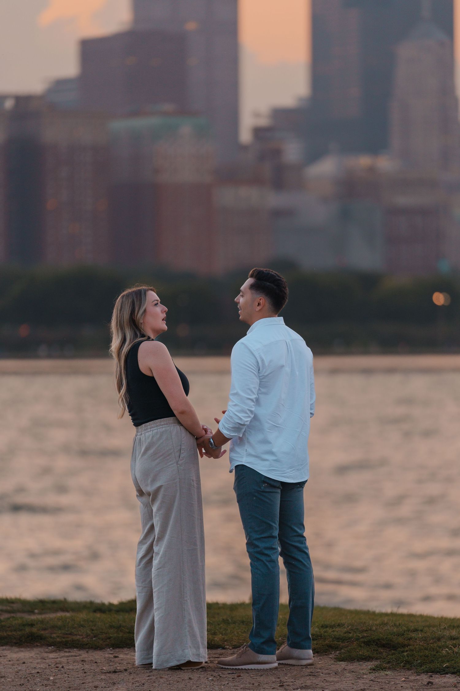 Couple holding hands and gazing at each other by Lake Michigan with the Chicago skyline at twilight.