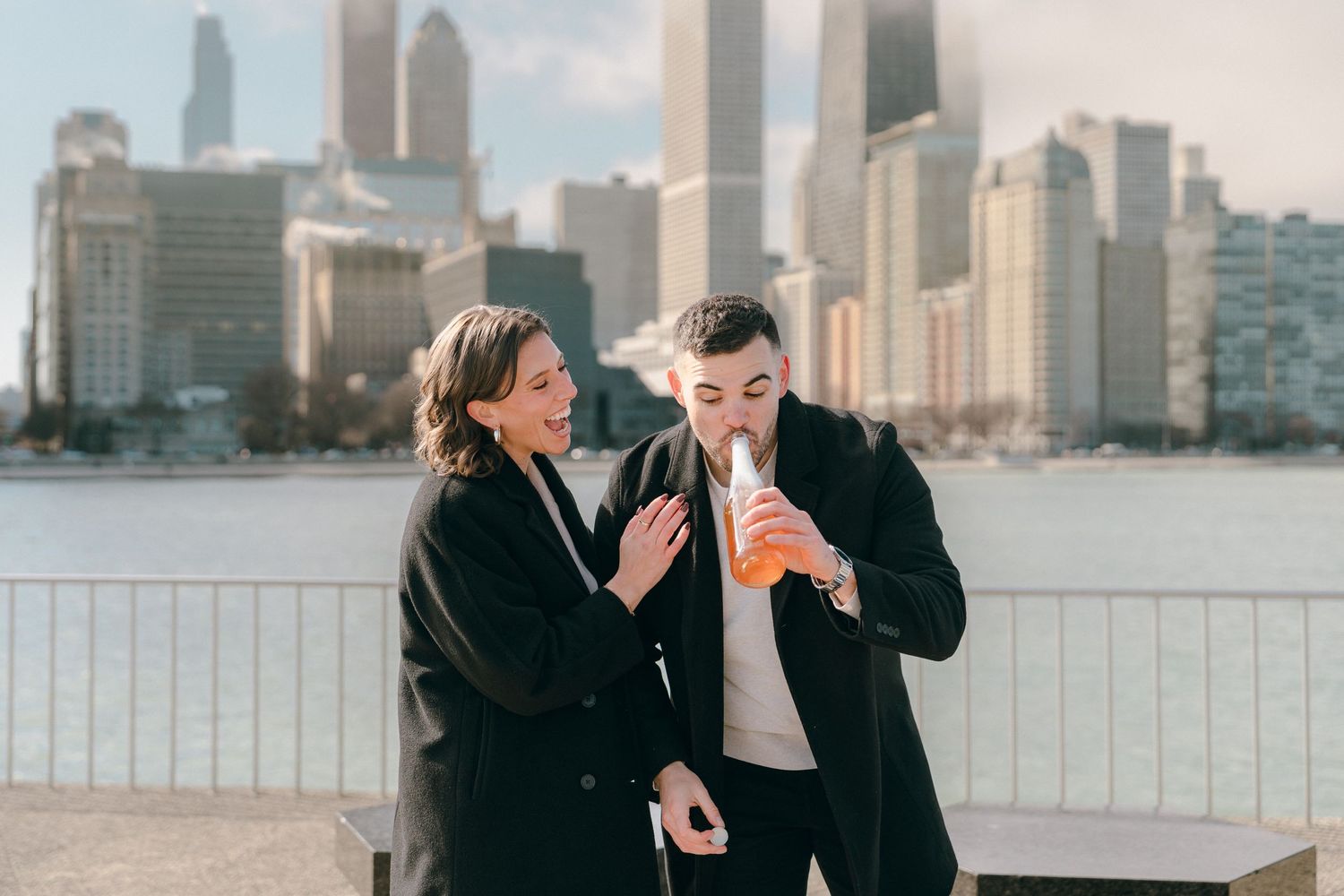 Couple sharing champagne bottle outdoors with Chicago city skyline in background.