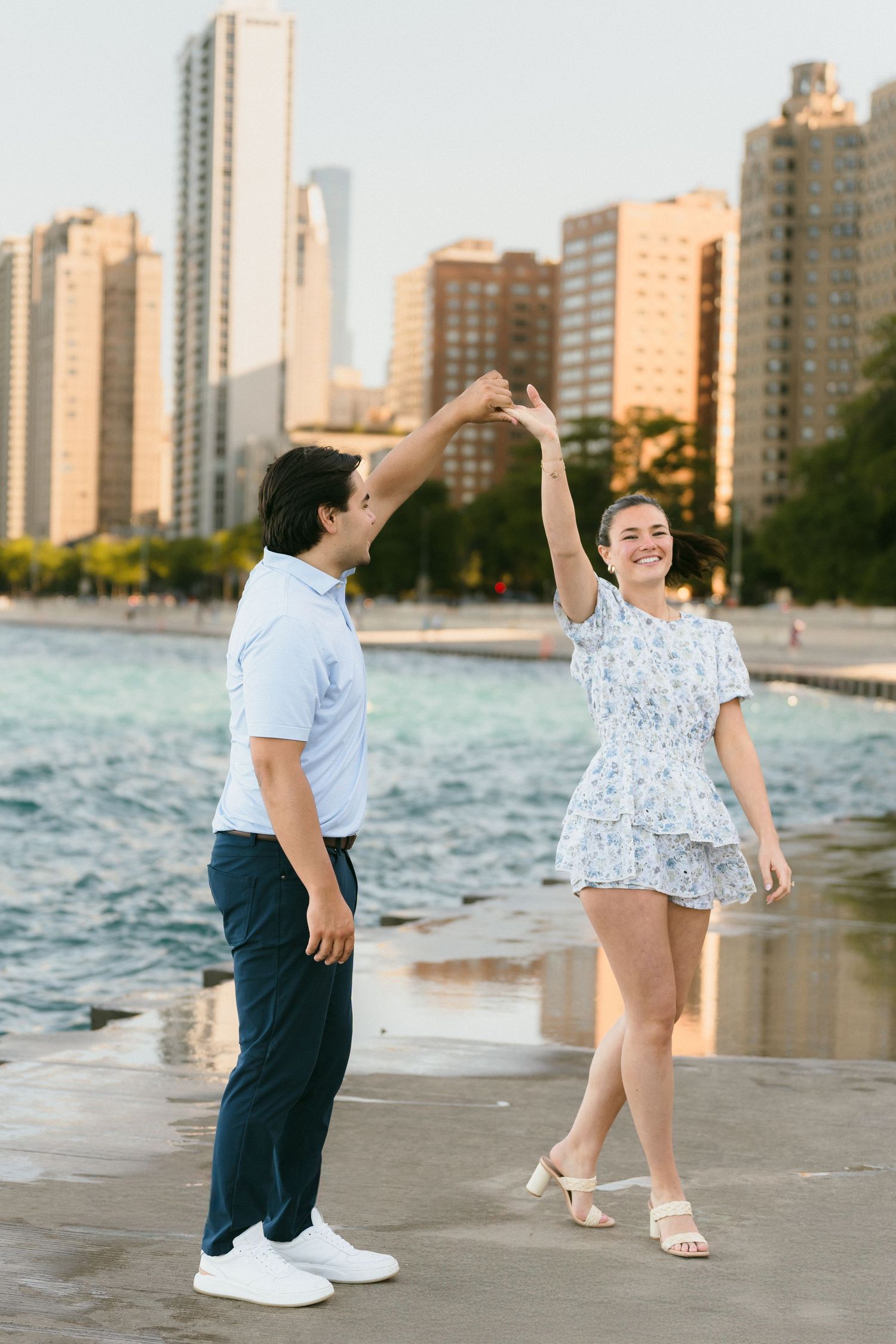 Happy couple dancing and spinning by the waterfront with Chicago city skyline glowing in golden sunset light.