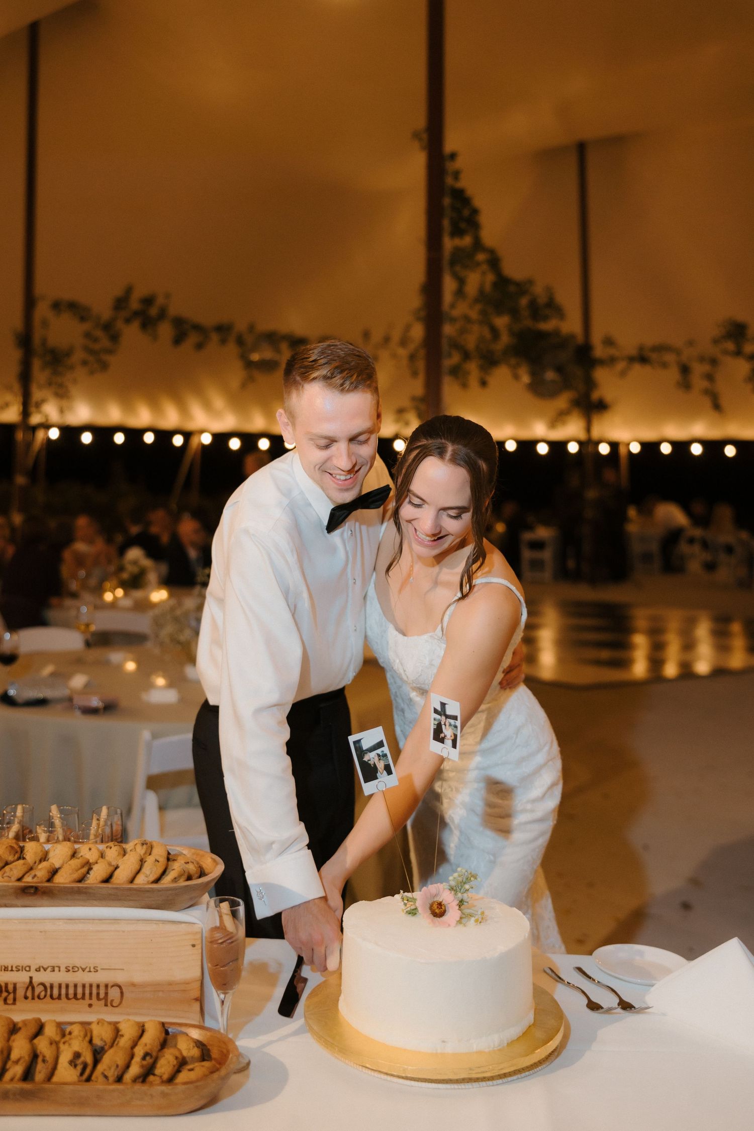 Happy bride and groom cutting their elegant white wedding cake at a tented outdoor reception.