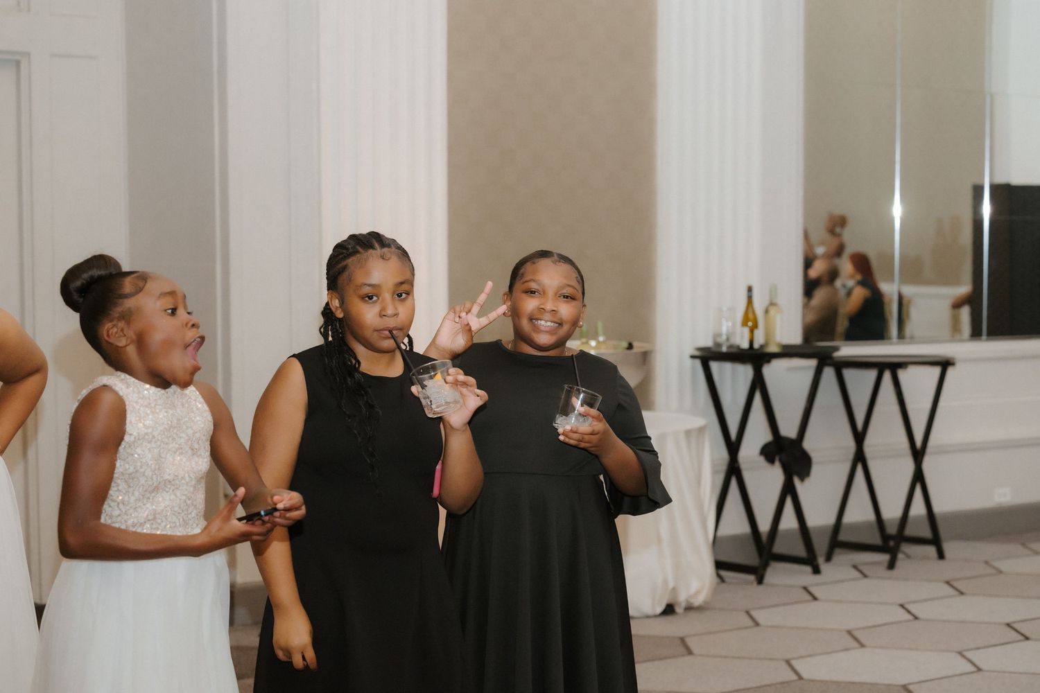 Three young girls in formal attire pose and smile at an elegant wedding reception venue.