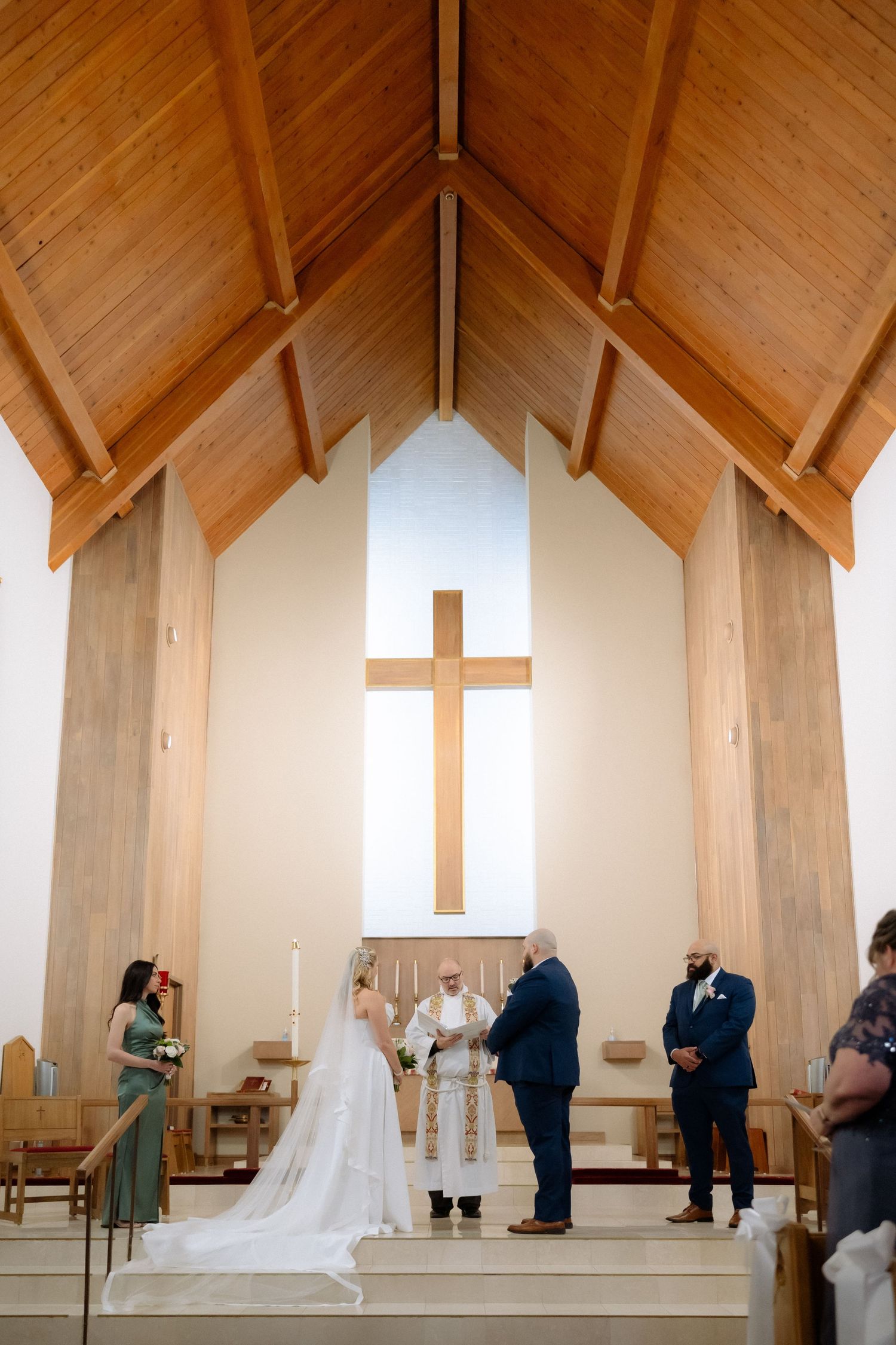 Bride and groom exchange vows at a church altar with a wooden cross and vaulted ceiling during a wedding ceremony.