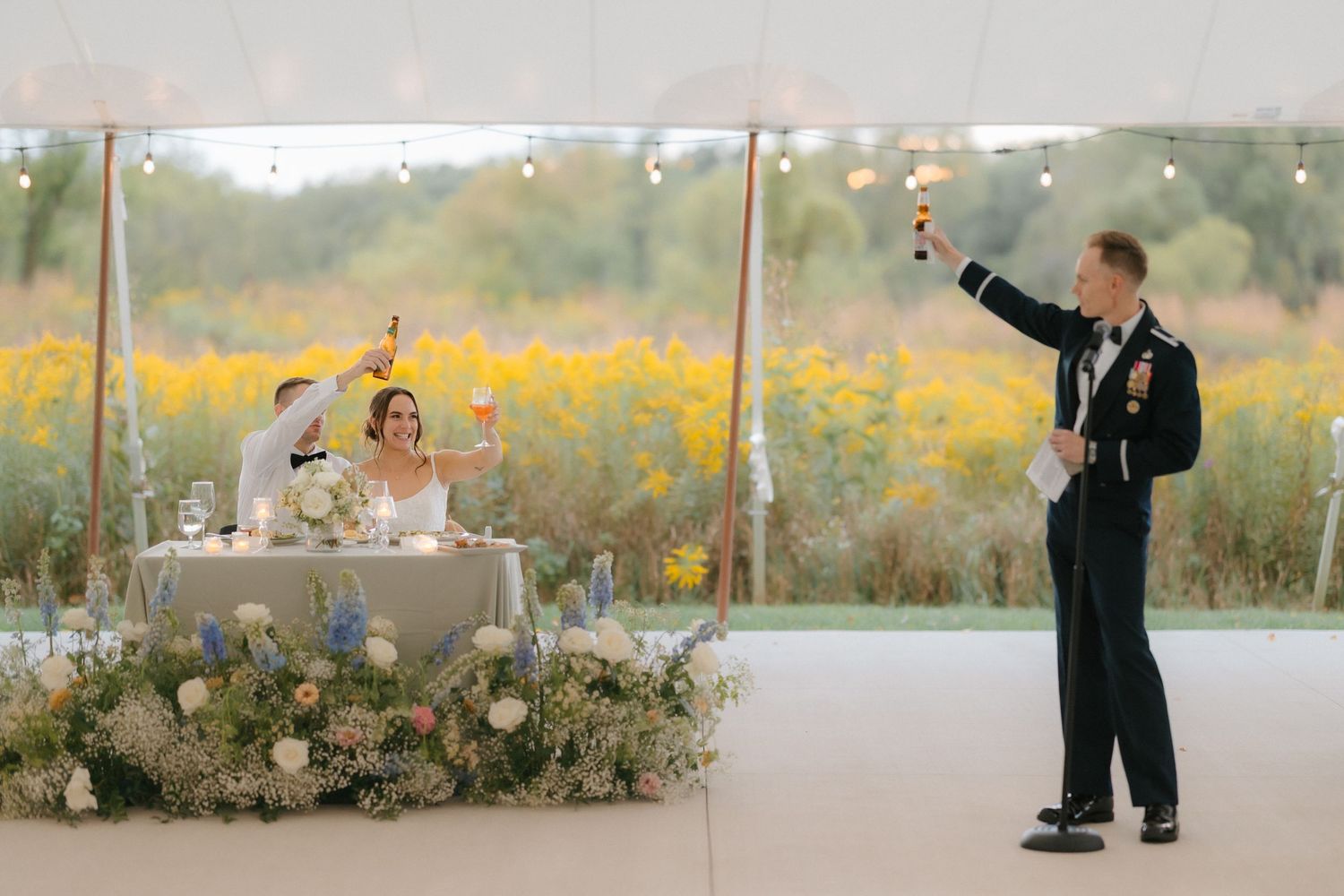 Military officer raises a champagne toast to the newlyweds at their sweetheart table during the wedding reception.