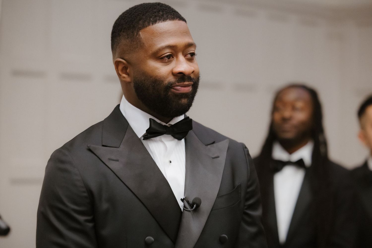 Elegant man in black tuxedo with bow tie at formal event, smiling confidently.