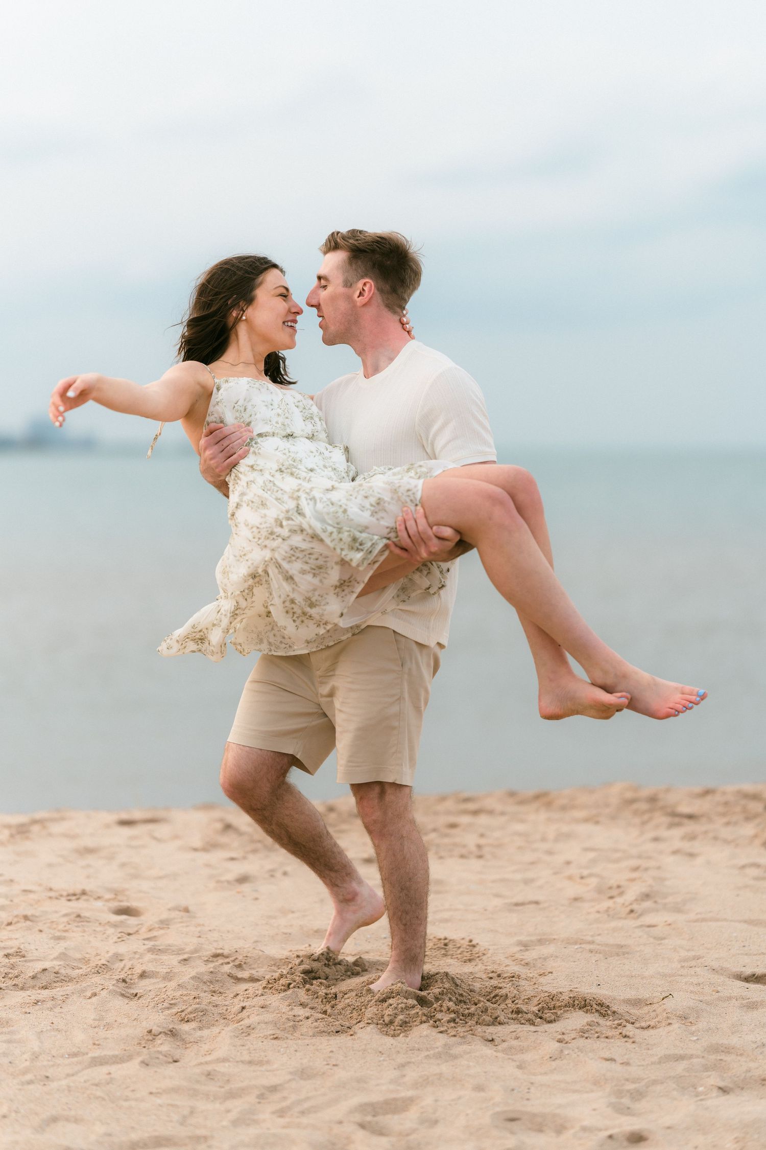 Man carrying woman in his arms on a sandy beach, couple gazing at each other near the ocean.