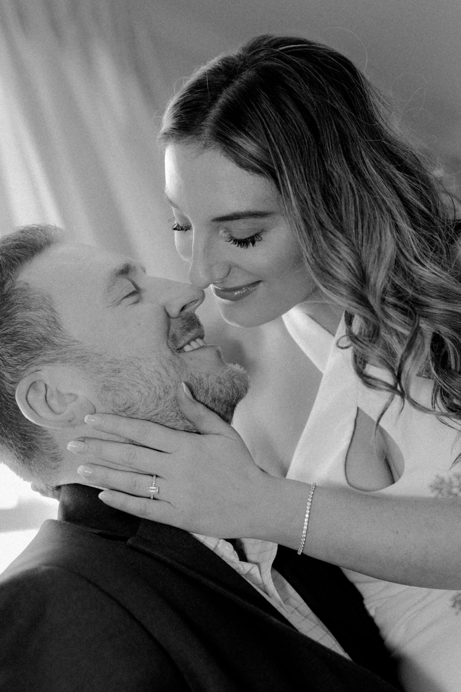 Black and white romantic portrait of bride tenderly holding groom's face as they share a moment.