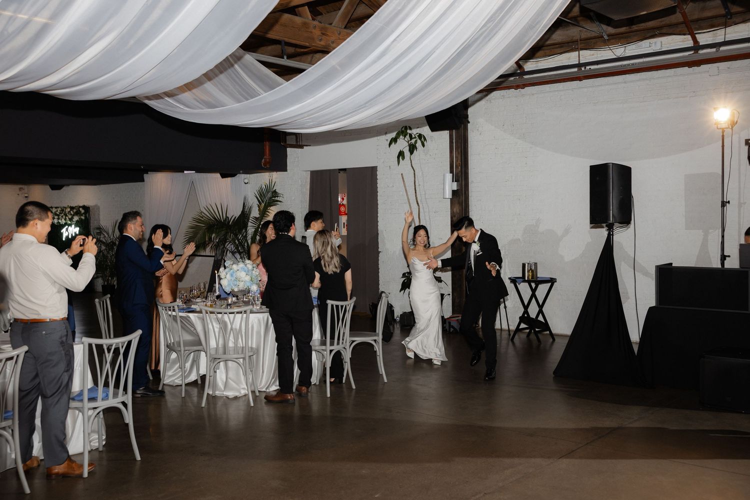 Bride and groom share first dance at elegant wedding reception with white draped ceiling and silver decor.
